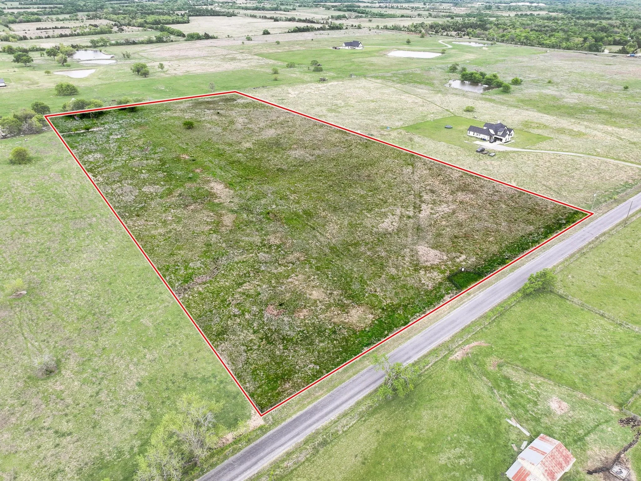 Expansive undeveloped land parcel featuring a visible road frontage, perimeter boundary marking, and a mix of grass and natural ground cover