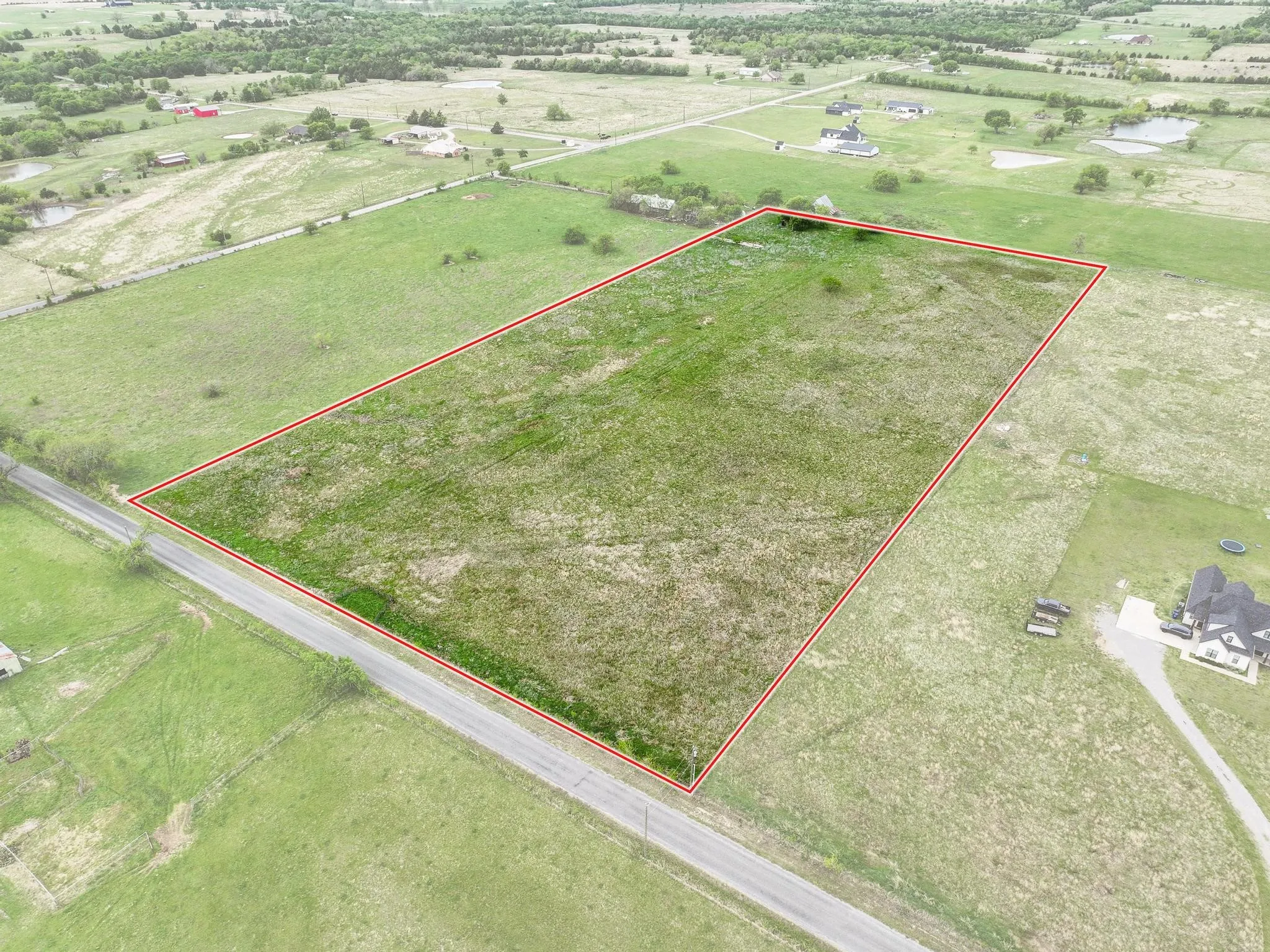Expansive parcel of land featuring a predominantly flat topography, open grassy areas, and direct road frontage