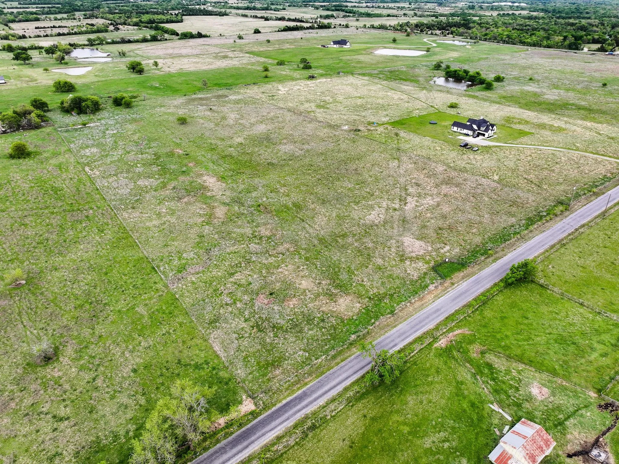 Expansive rural property featuring a long paved road frontage, mature trees, and multiple ponds