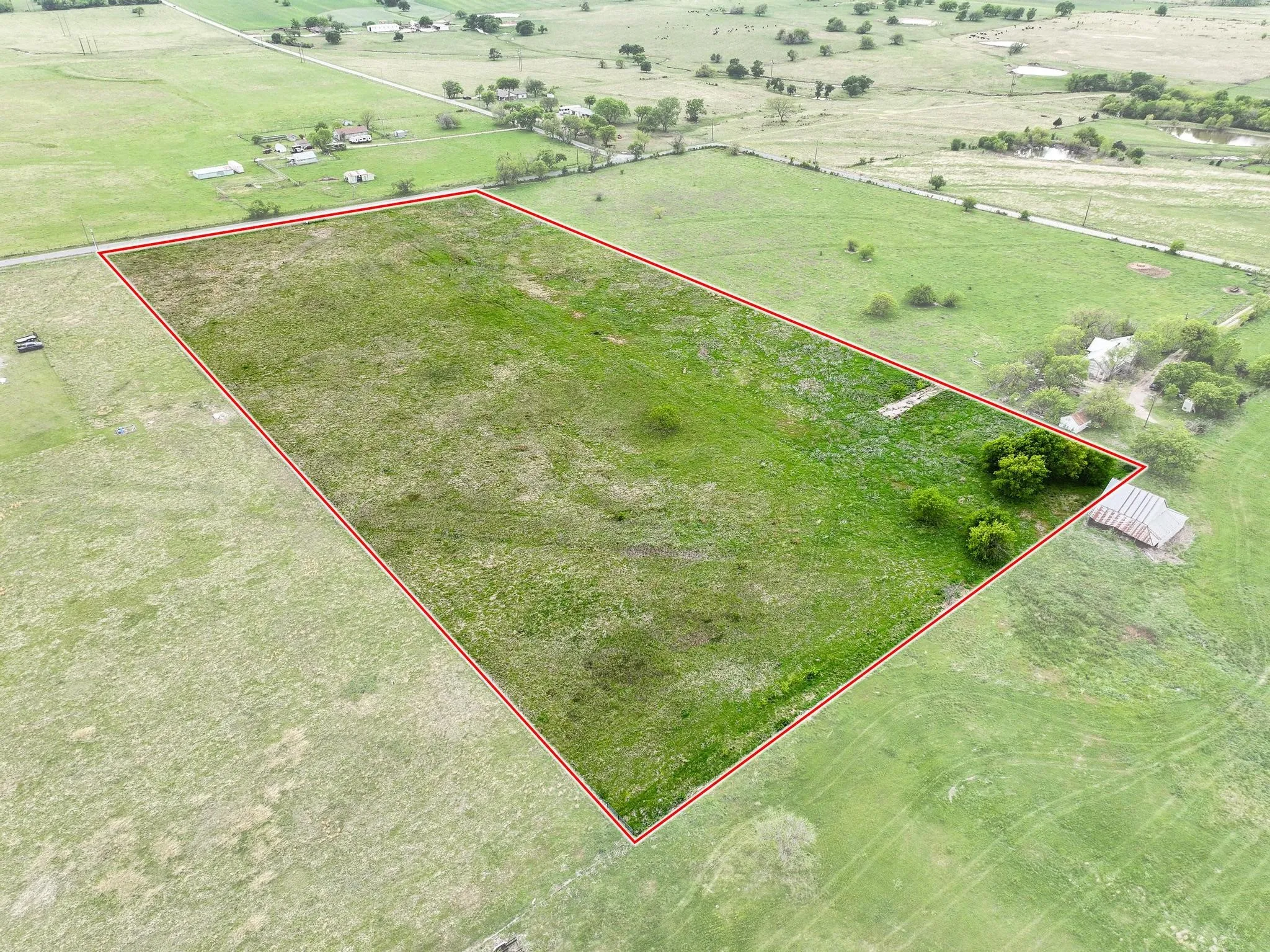 Expansive rural acreage featuring green pastures, scattered mature trees, and an agricultural outbuilding