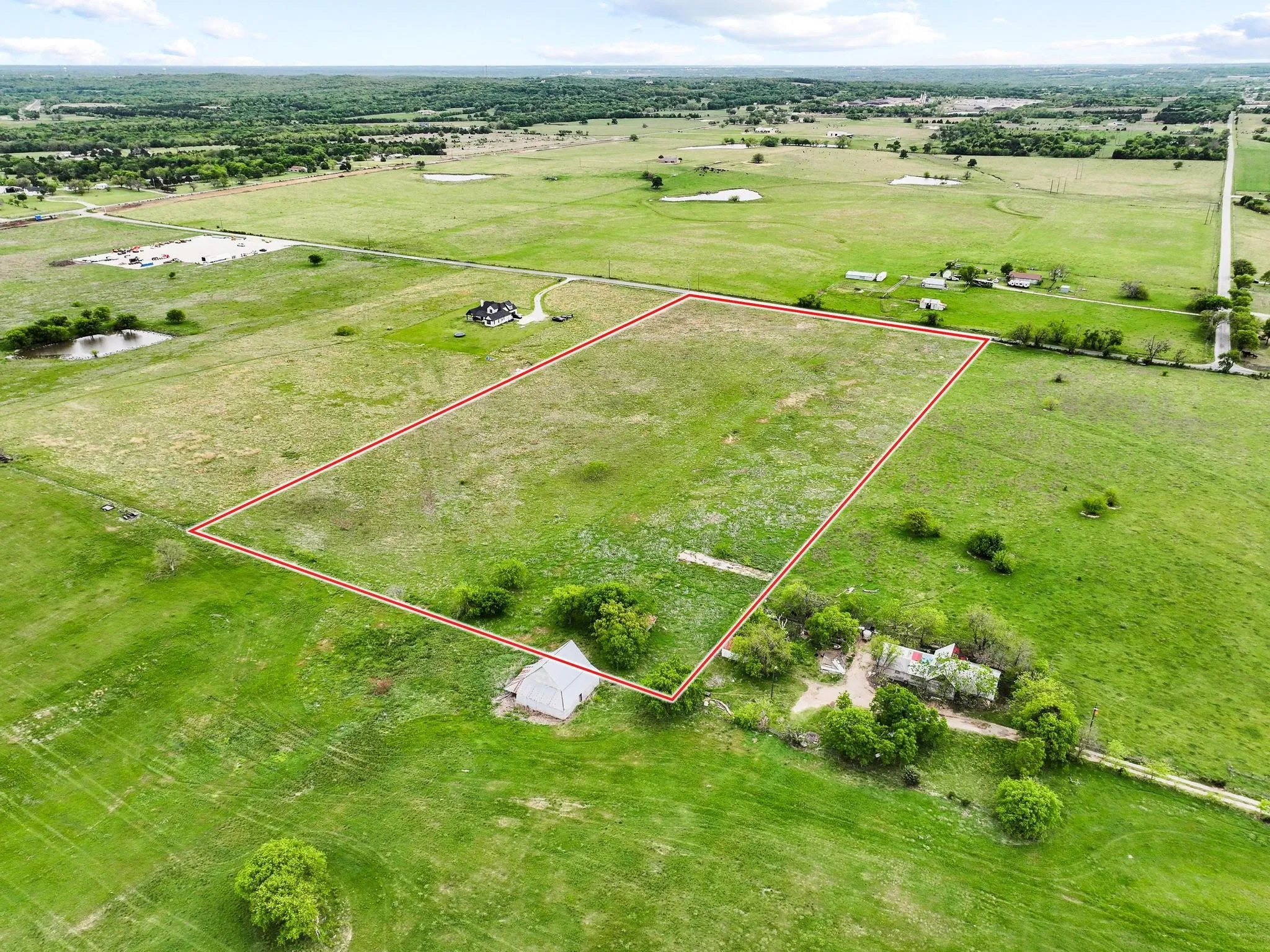 Expansive green acreage with a defined perimeter, surrounded by additional green fields and distant wooded areas