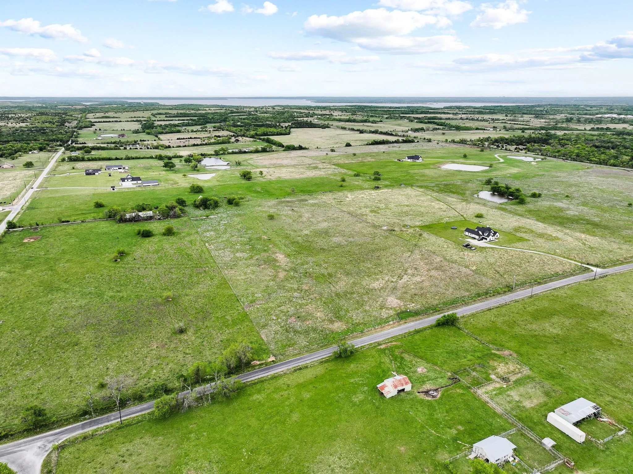 Expansive rural landscape featuring a mix of open fields, scattered trees, and multiple residential properties