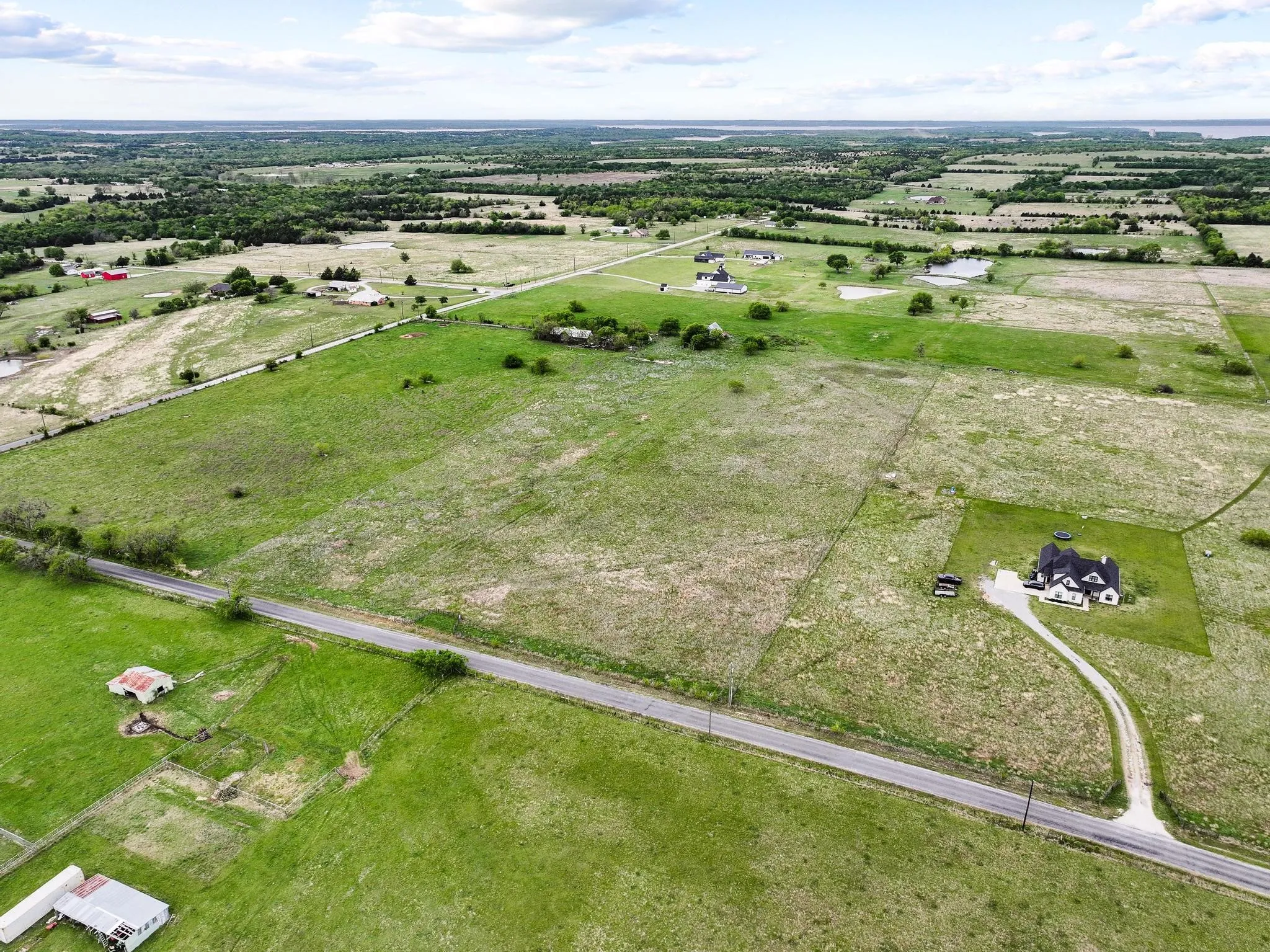 Expansive rural landscape featuring a single-family residence with a black roof, a gravel driveway, and surrounding green fields