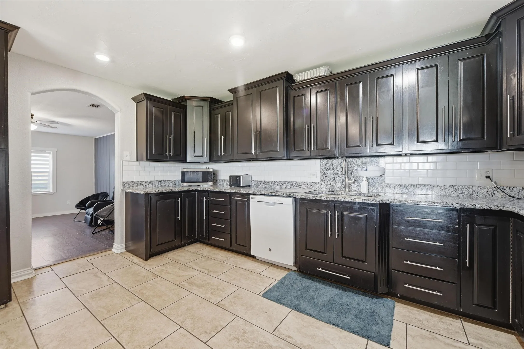Kitchen featuring backsplash, arched walkways, white dishwasher, light stone countertops, and stainless steel microwave