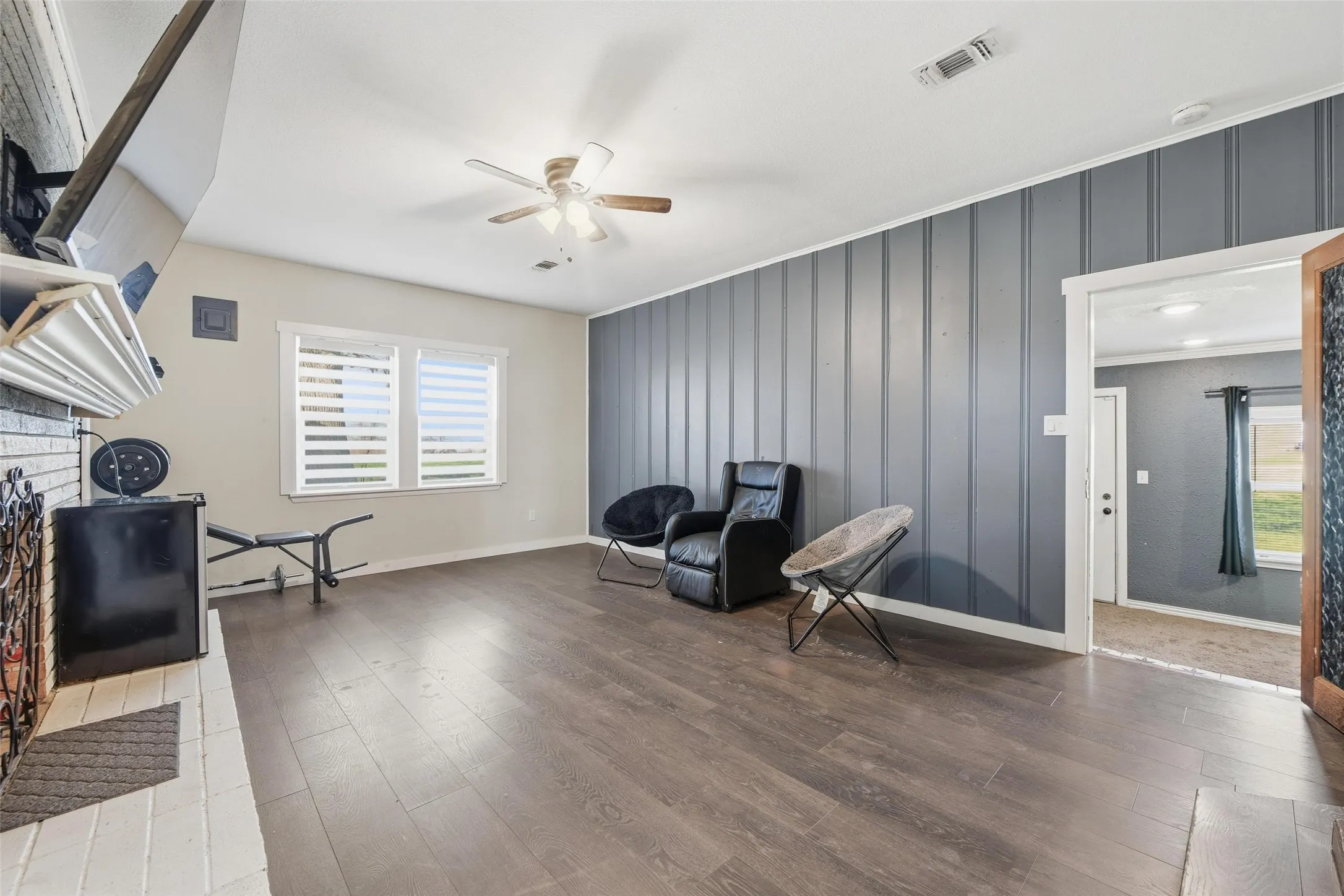 Living area featuring dark wood finished floors, plenty of natural light, an accent wall, a ceiling fan, and a decorative wall