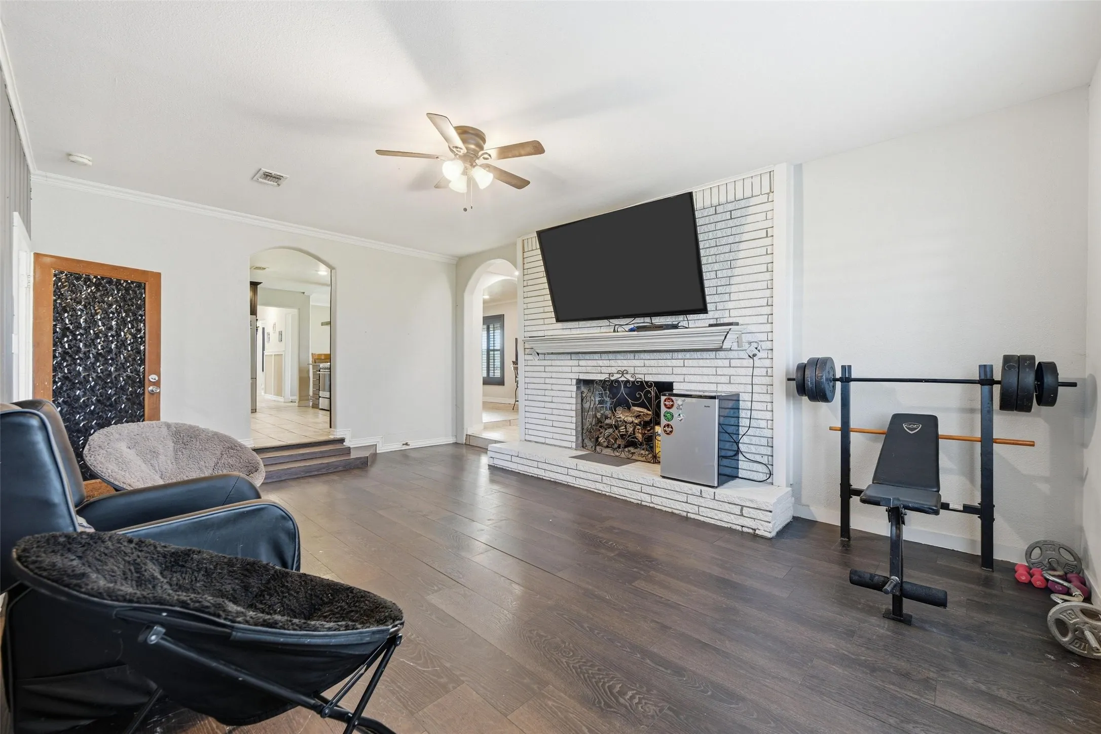 Living room with wood finished floors, a ceiling fan, a fireplace, arched walkways, and ornamental molding