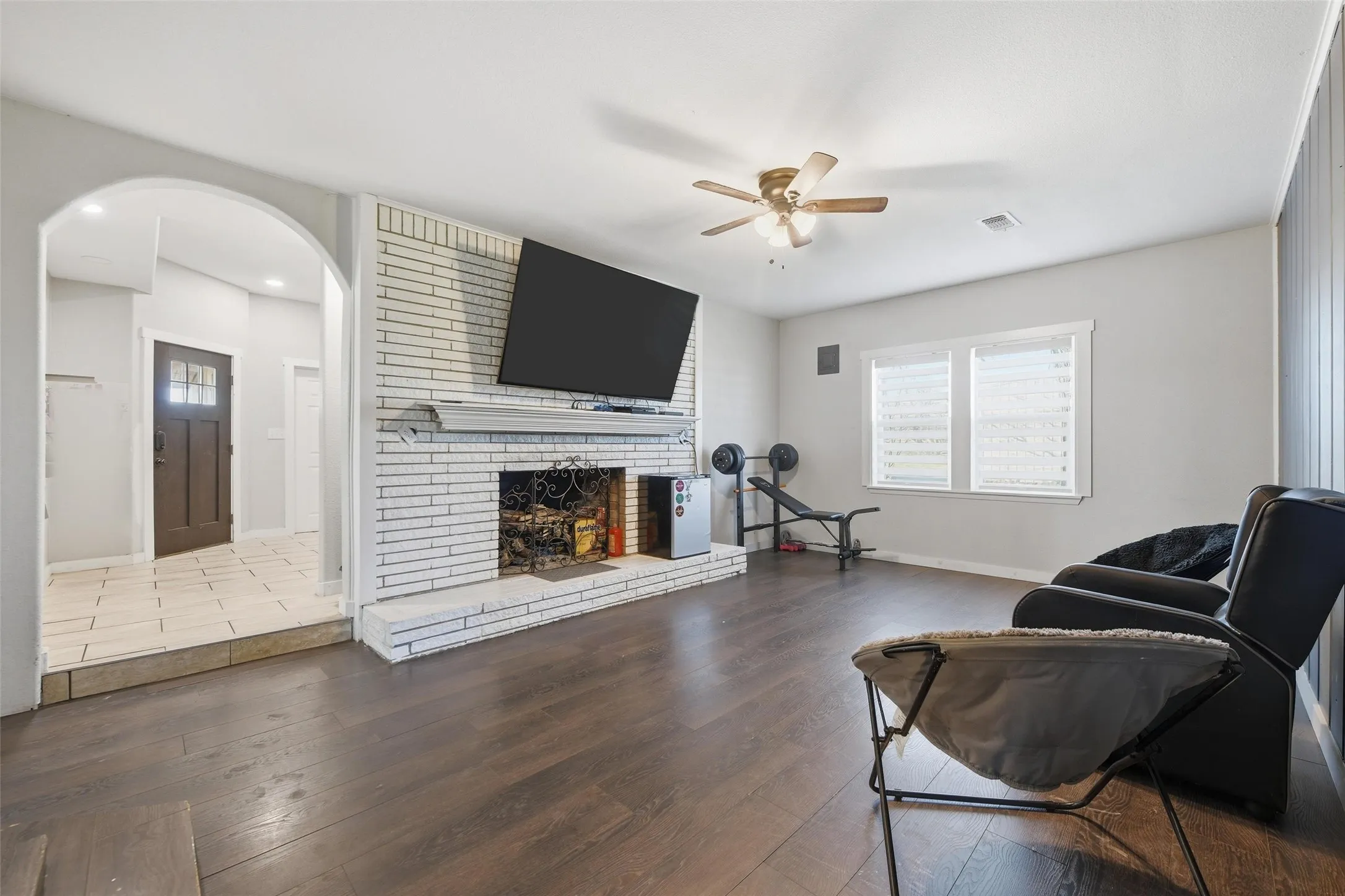 Living area featuring hardwood / wood-style floors, ceiling fan, a brick fireplace, and arched walkways
