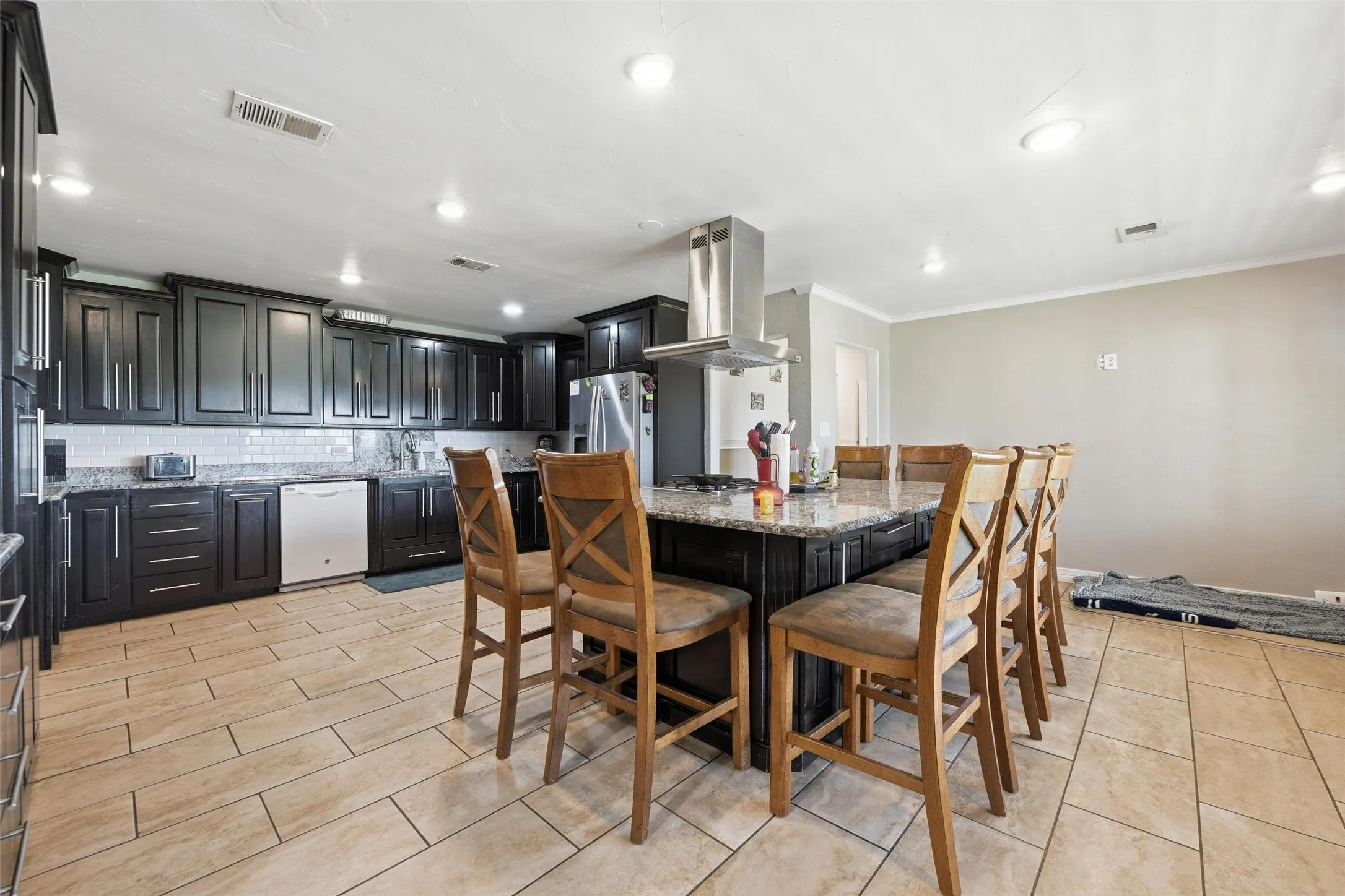 Kitchen with dark cabinets, light stone counters, tasteful backsplash, a kitchen breakfast bar, and extractor fan