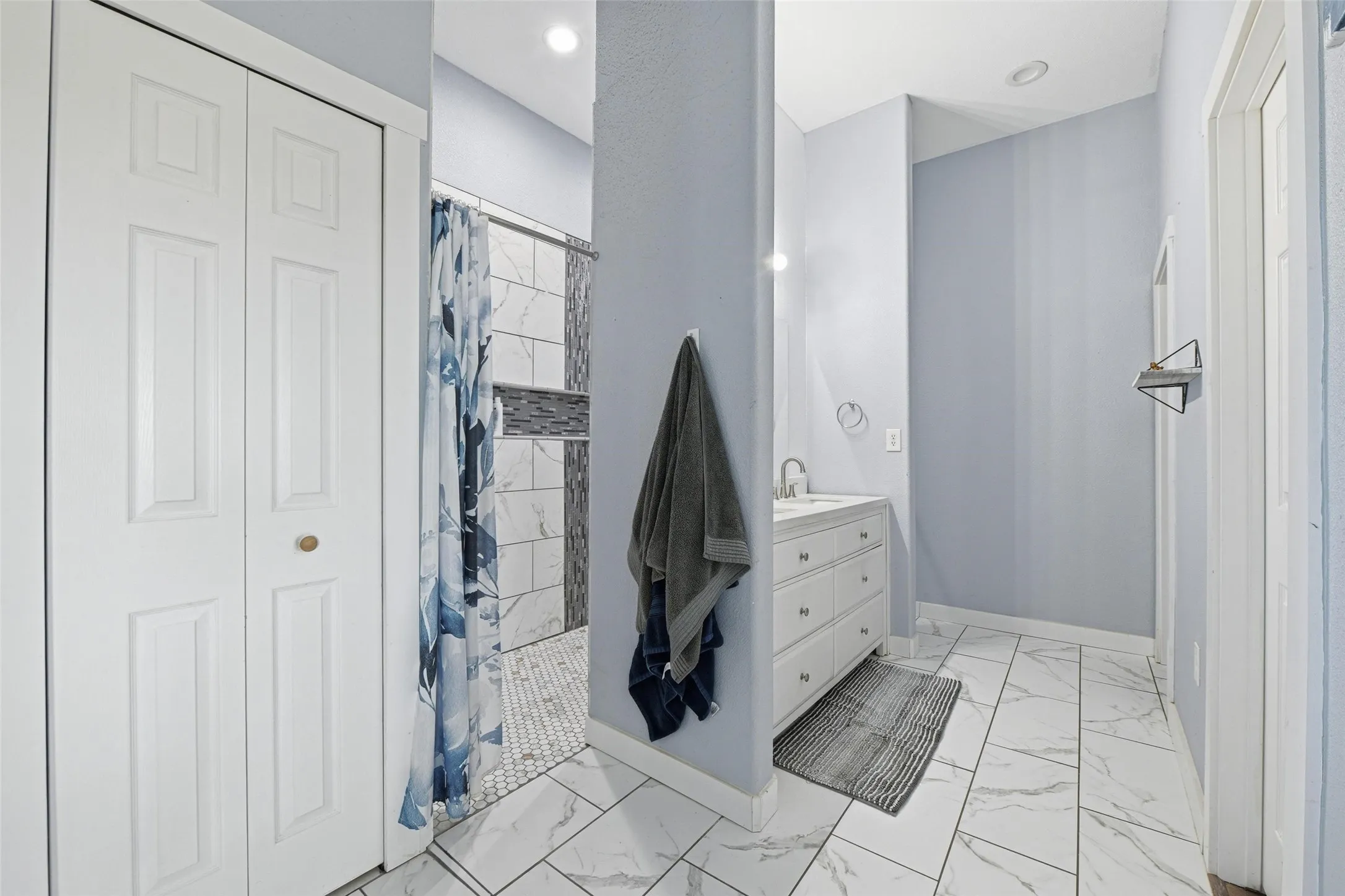 Bathroom with vanity, light marble finish flooring, a closet, and tiled shower