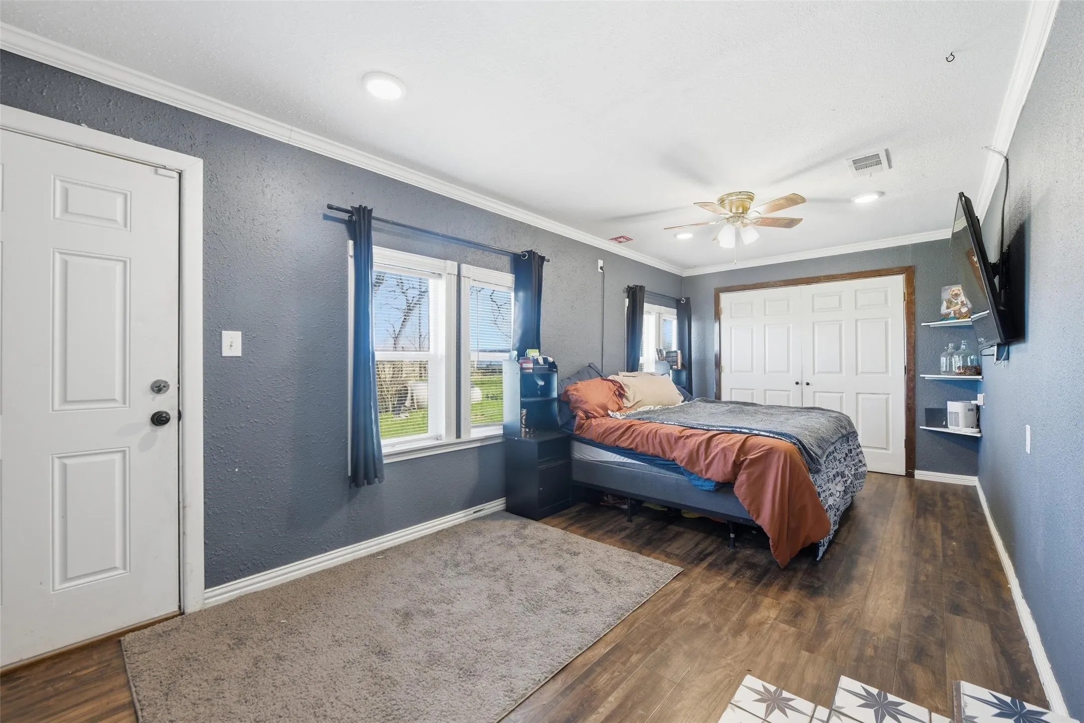 Bedroom featuring crown molding, a closet, dark wood finished floors, a textured wall, and ceiling fan