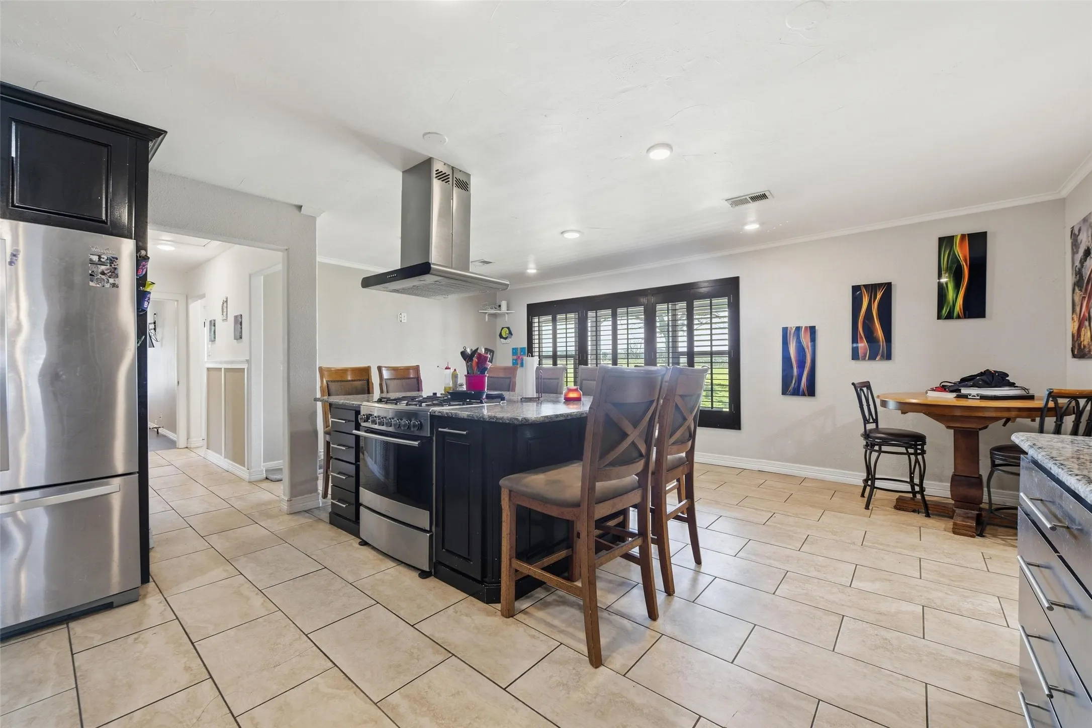 Kitchen with dark cabinets, stainless steel appliances, island exhaust hood, dark stone countertops, and a kitchen island