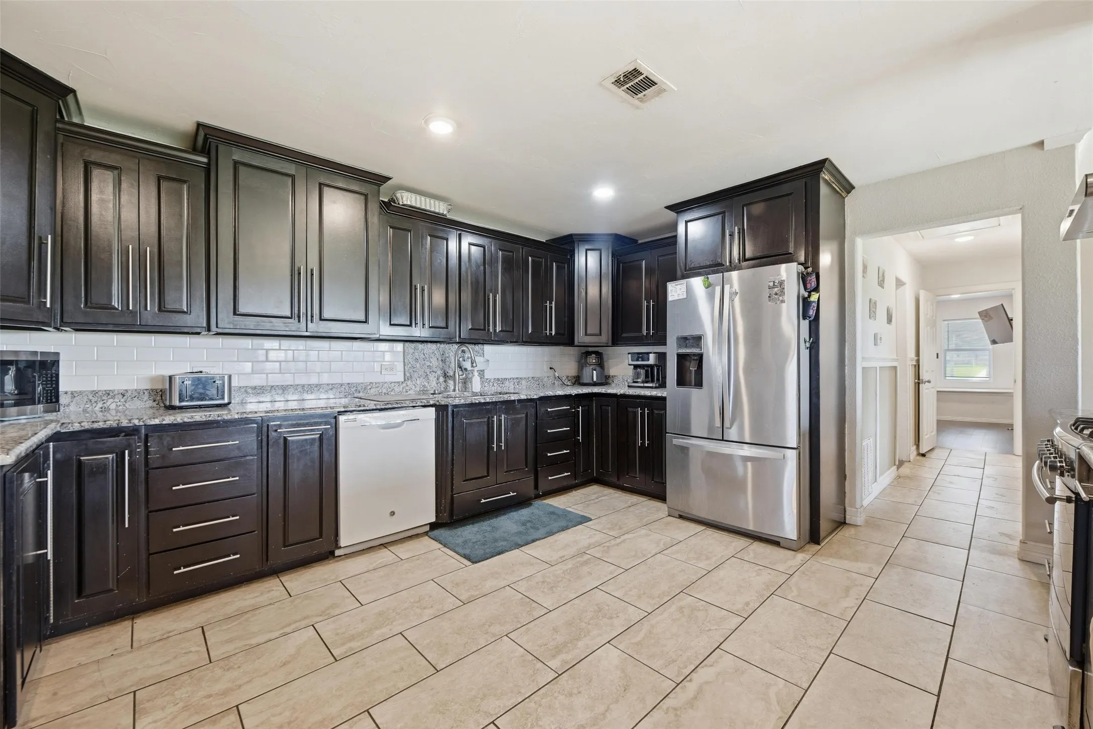 Kitchen with stainless steel appliances, light stone countertops, backsplash, dark wood finish cabinetry, and recessed lighting