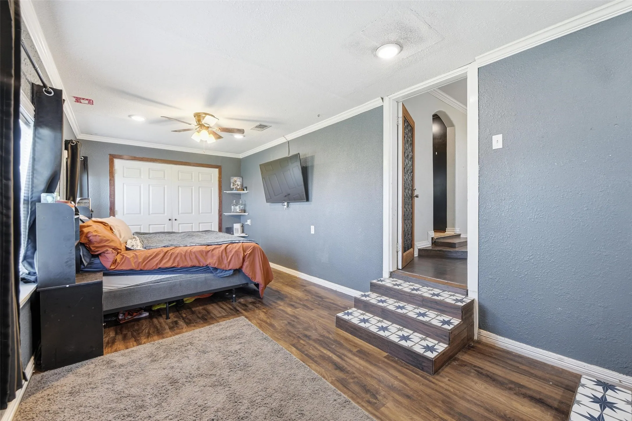 Bedroom featuring arched walkways, a closet, dark wood-style flooring, ornamental molding, and a ceiling fan