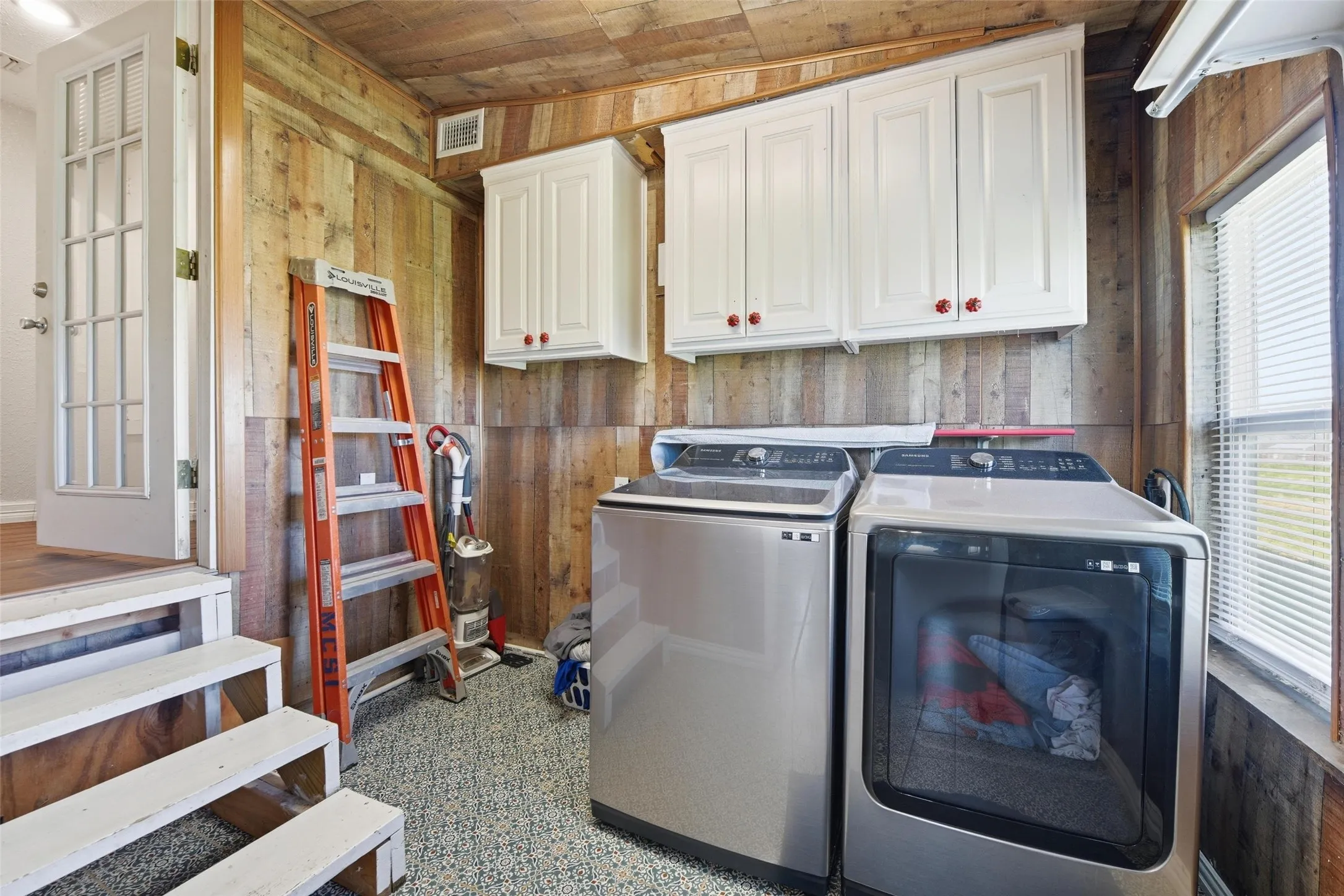 Laundry area with wood walls, wood ceiling, washer and dryer, and cabinet space