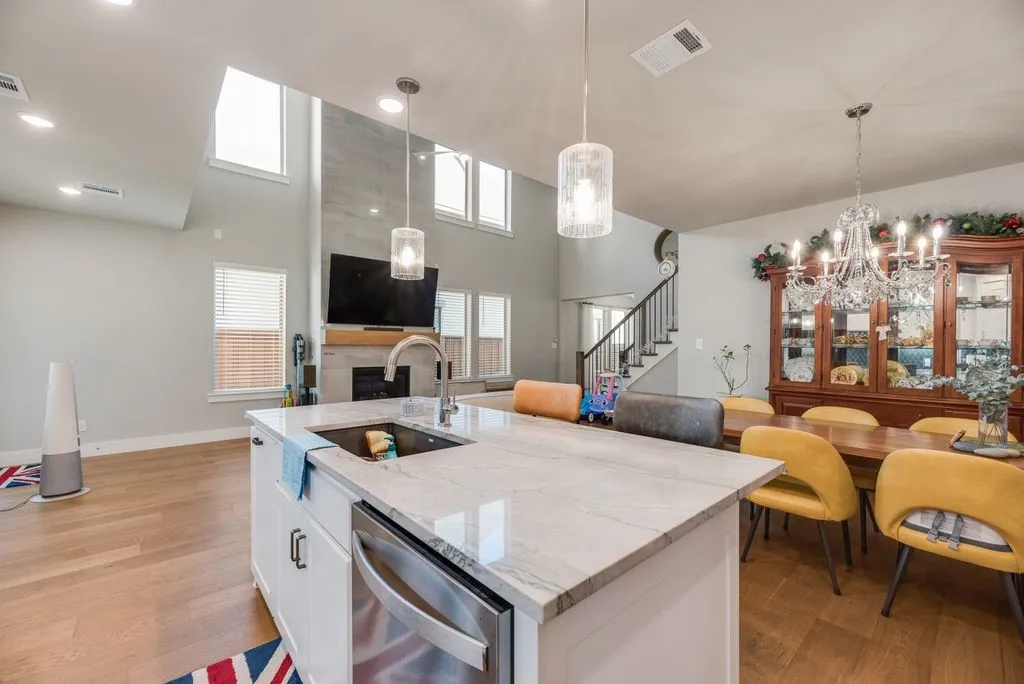 Kitchen with light stone counters, a high ceiling, white cabinets, light wood-style floors, and stainless steel dishwasher