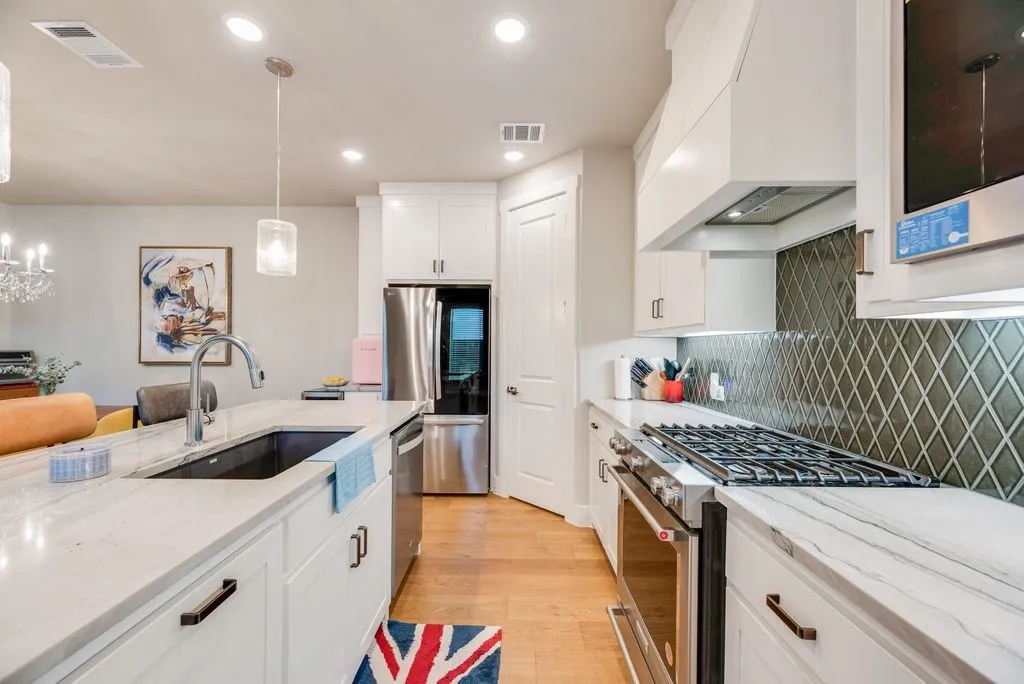 Kitchen with stainless steel appliances, white cabinets, light stone counters, light wood-type flooring, and hanging light fixtures