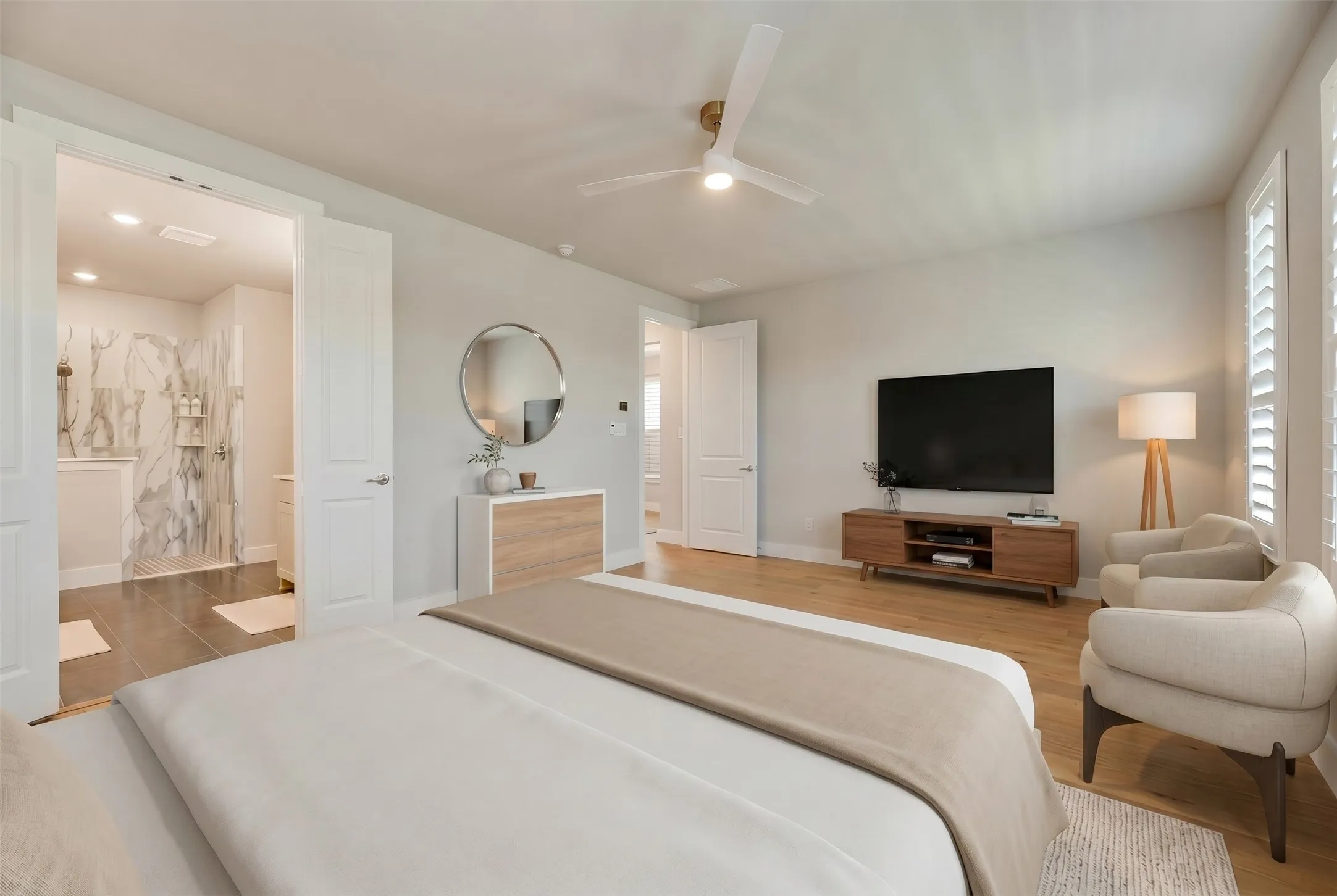 Bright sleeping area with light wood-finish flooring, a ceiling fan, and window shutters