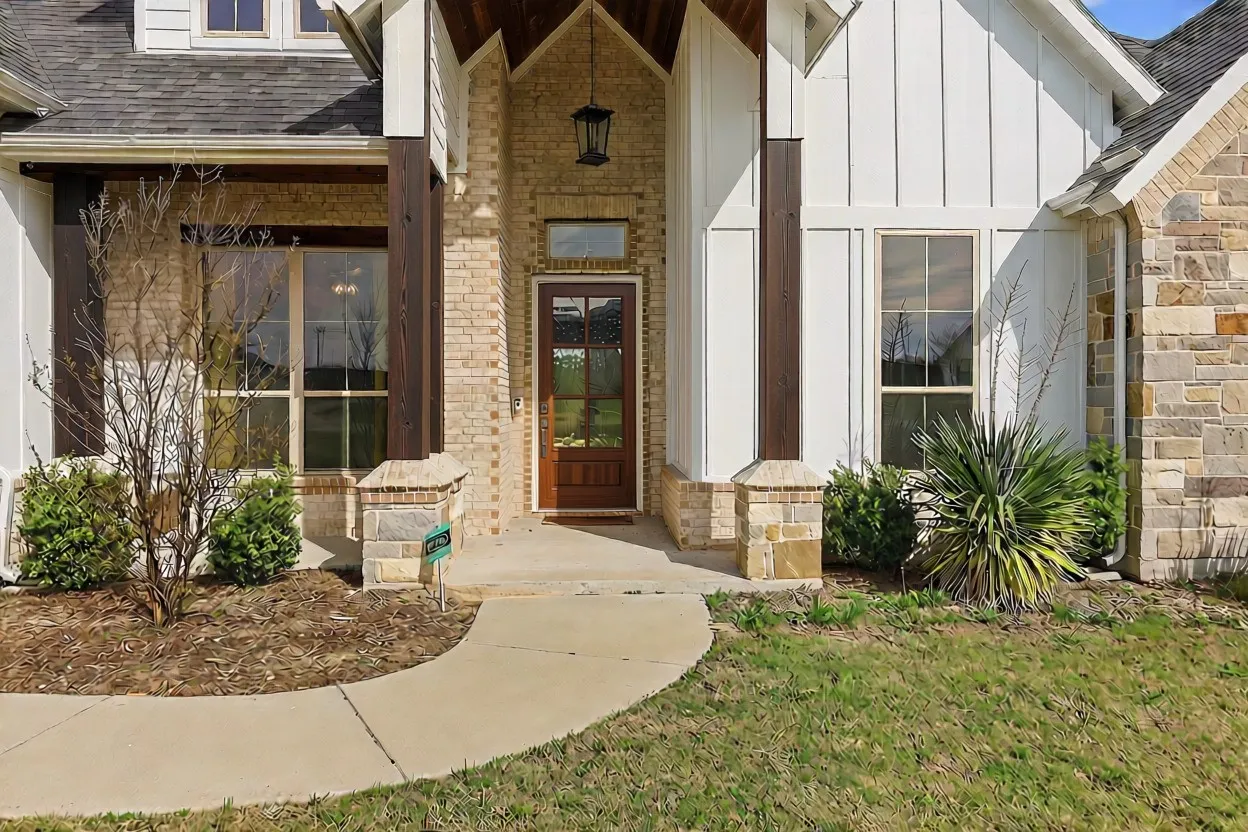 Crafted entryway featuring a wood-panel door, brick and stone facade, vertical white siding, dark wood support beams, and a concrete pathway