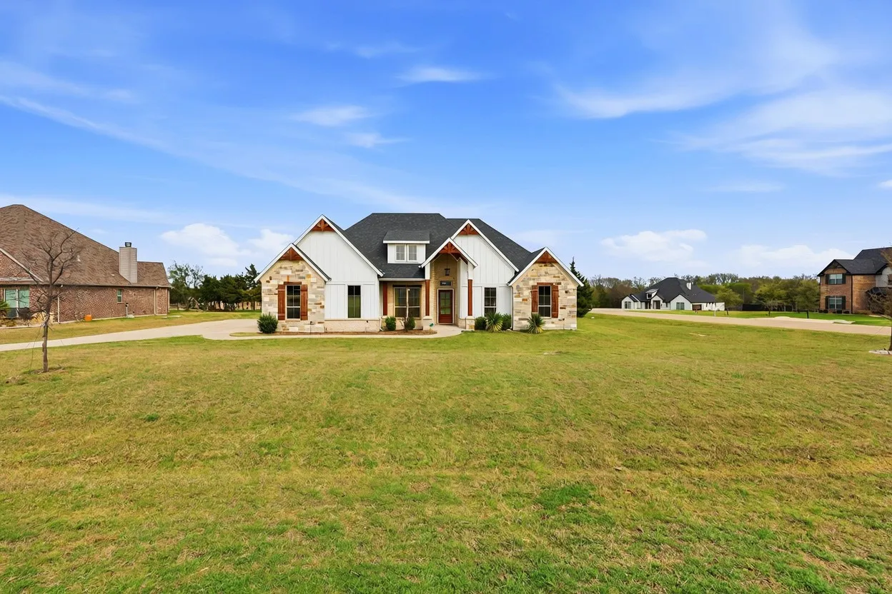 Contemporary ranch-style home featuring a stone and board-and-batten facade, dark shingle roof, and a prominent front entrance with a wooden double door