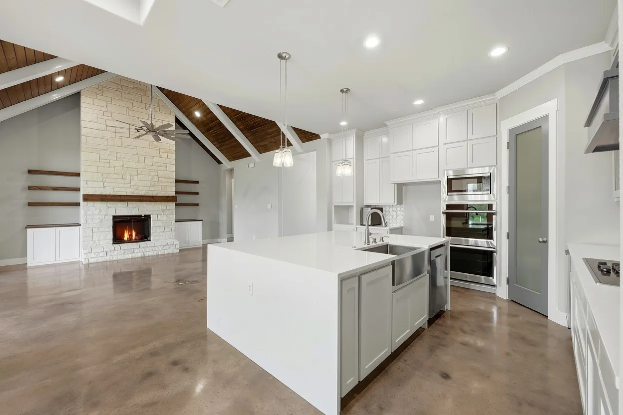 Open-concept living space featuring a stone-clad fireplace, vaulted ceiling with wood beams, and polished concrete flooring