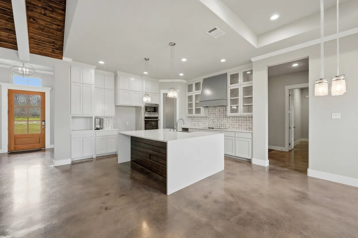 Open-concept kitchen featuring an oversized island with a white countertop and wood-finish paneling, white cabinetry, a decorative tile backsplash, and stainless steel appliances