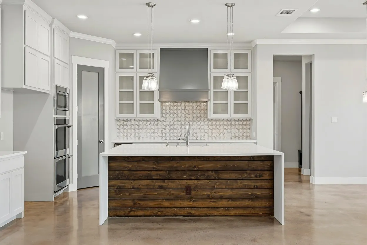 Kitchen featuring a central island with a wood-finish base and white countertop, stainless steel double ovens, white shaker cabinetry, glass-front upper cabinets, and a patterned tile backsplash