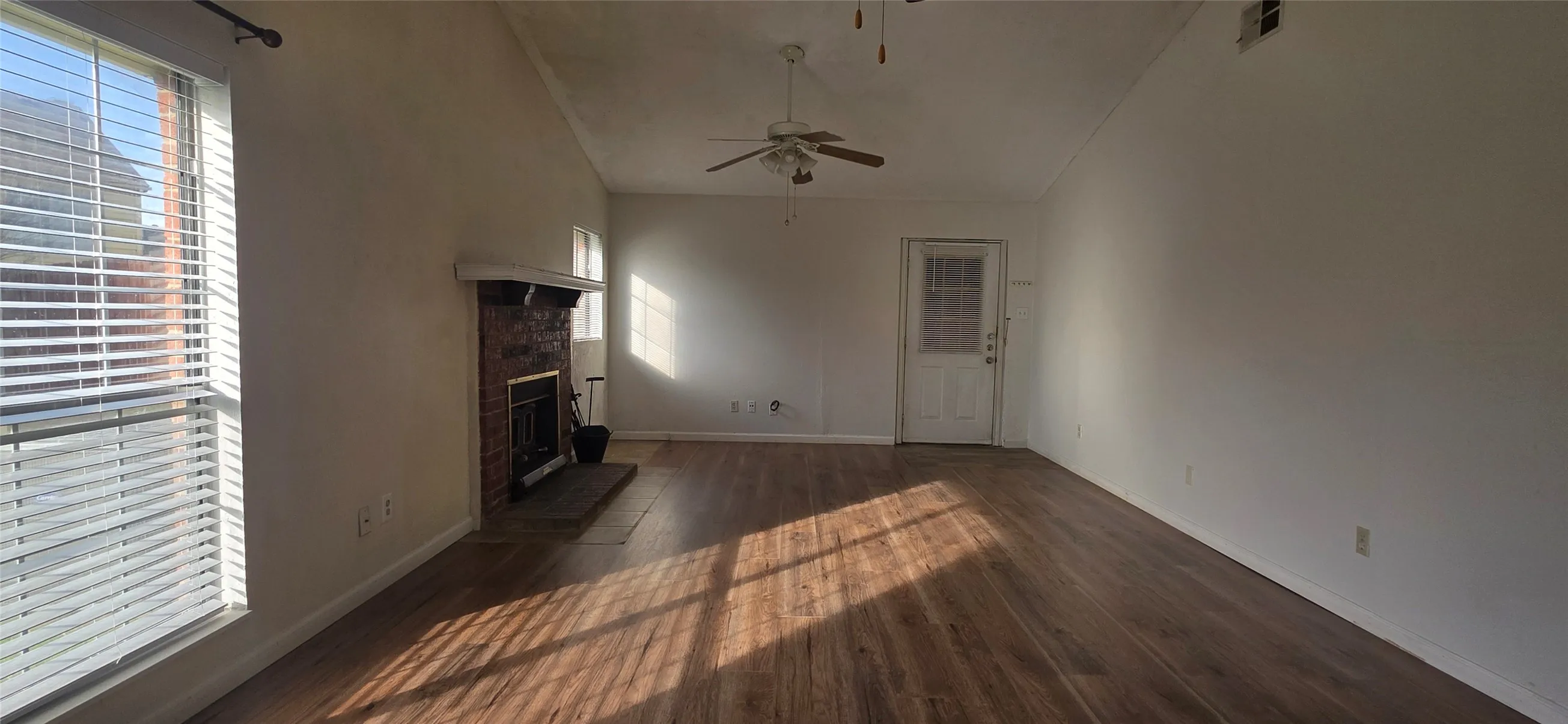 Unfurnished living room featuring dark wood-style flooring, a stone fireplace, vaulted ceiling, and a ceiling fan
