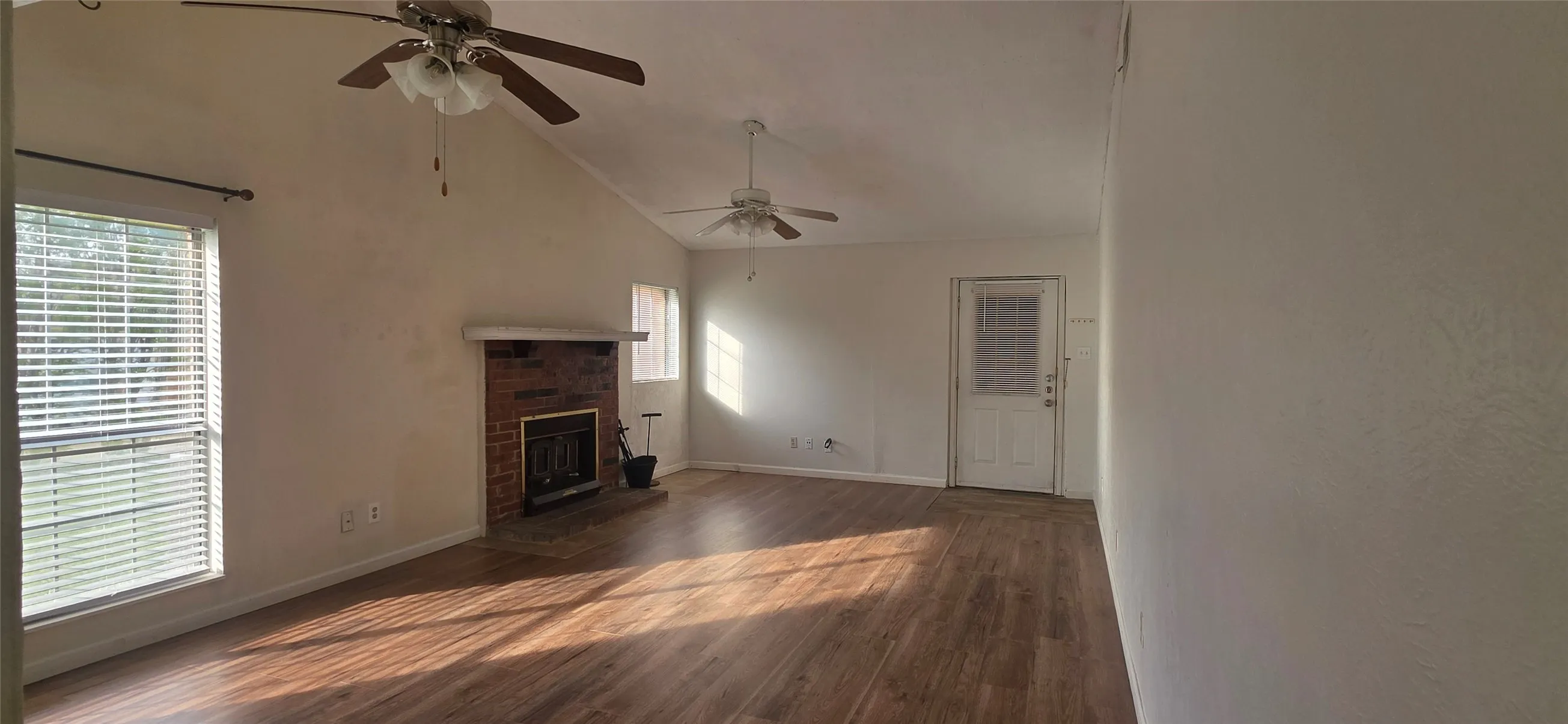 Unfurnished living room featuring vaulted ceiling, dark wood finished floors, a brick fireplace, and a ceiling fan