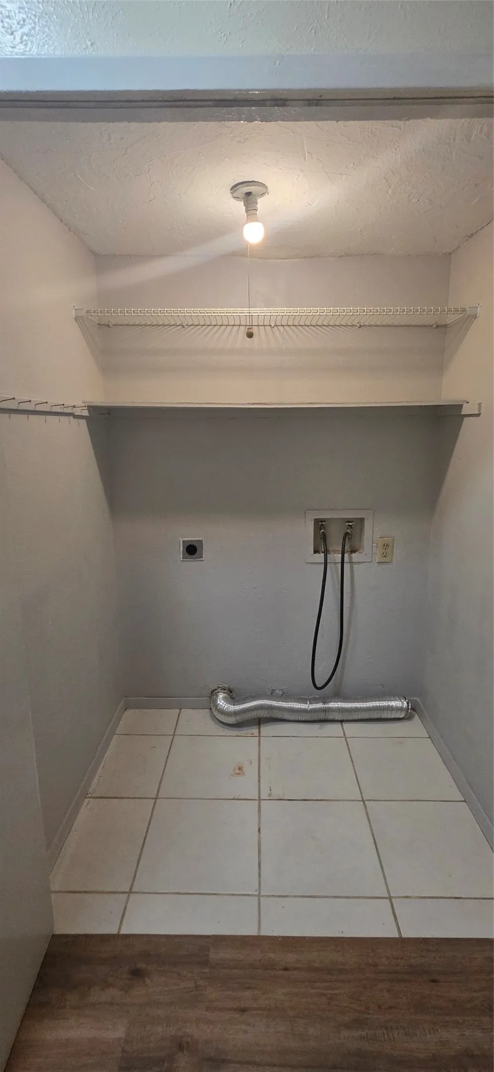Laundry room with hookup for an electric dryer, hookup for a washing machine, light tile patterned flooring, and a textured ceiling