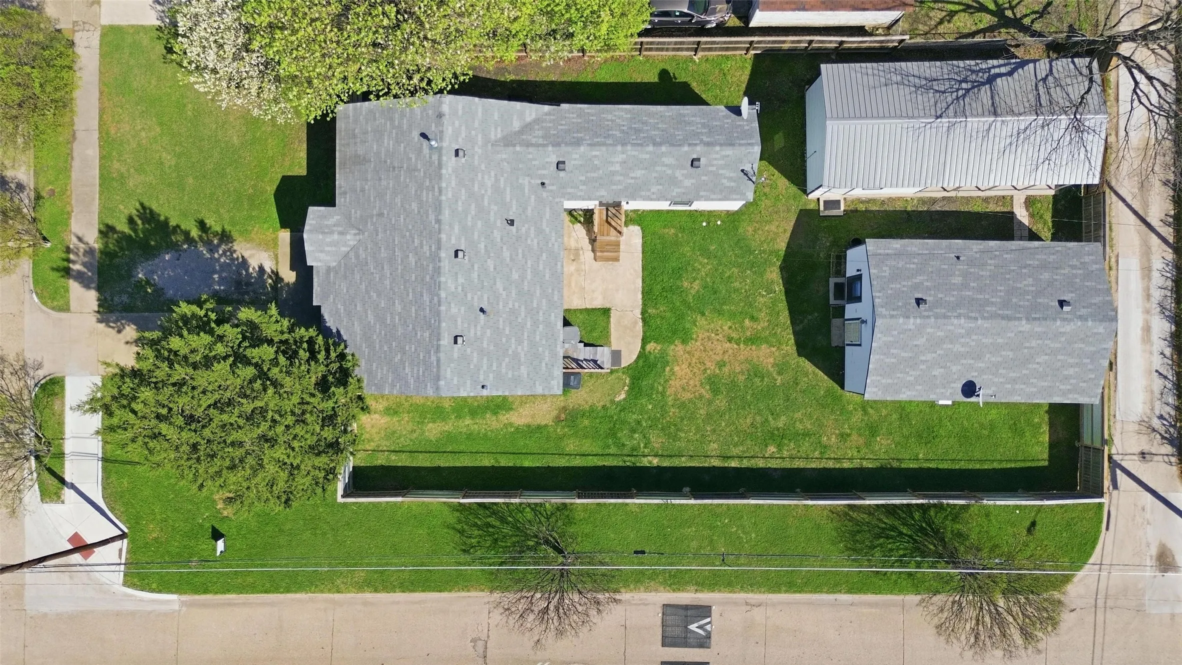 Spacious corner lot featuring a main residence with a gray shingle roof, a detached auxiliary building with a gray shingle roof, and a large metal-roofed structure