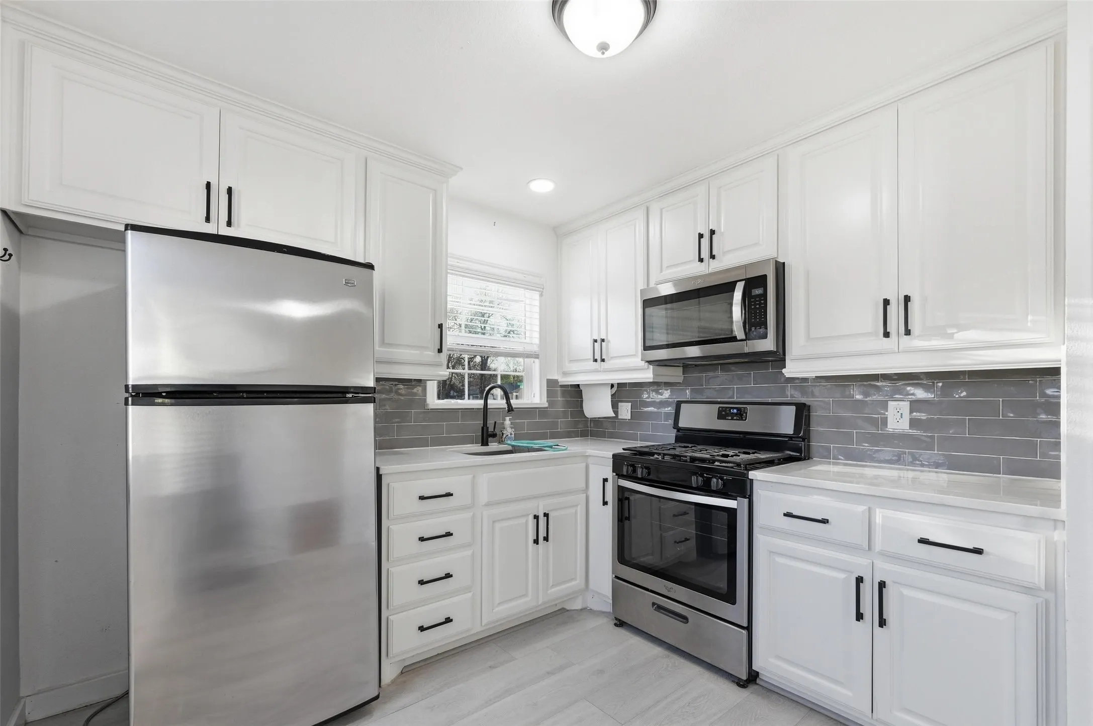 Kitchen featuring stainless steel appliances, white cabinets, recessed lighting, decorative backsplash, and light wood-type flooring