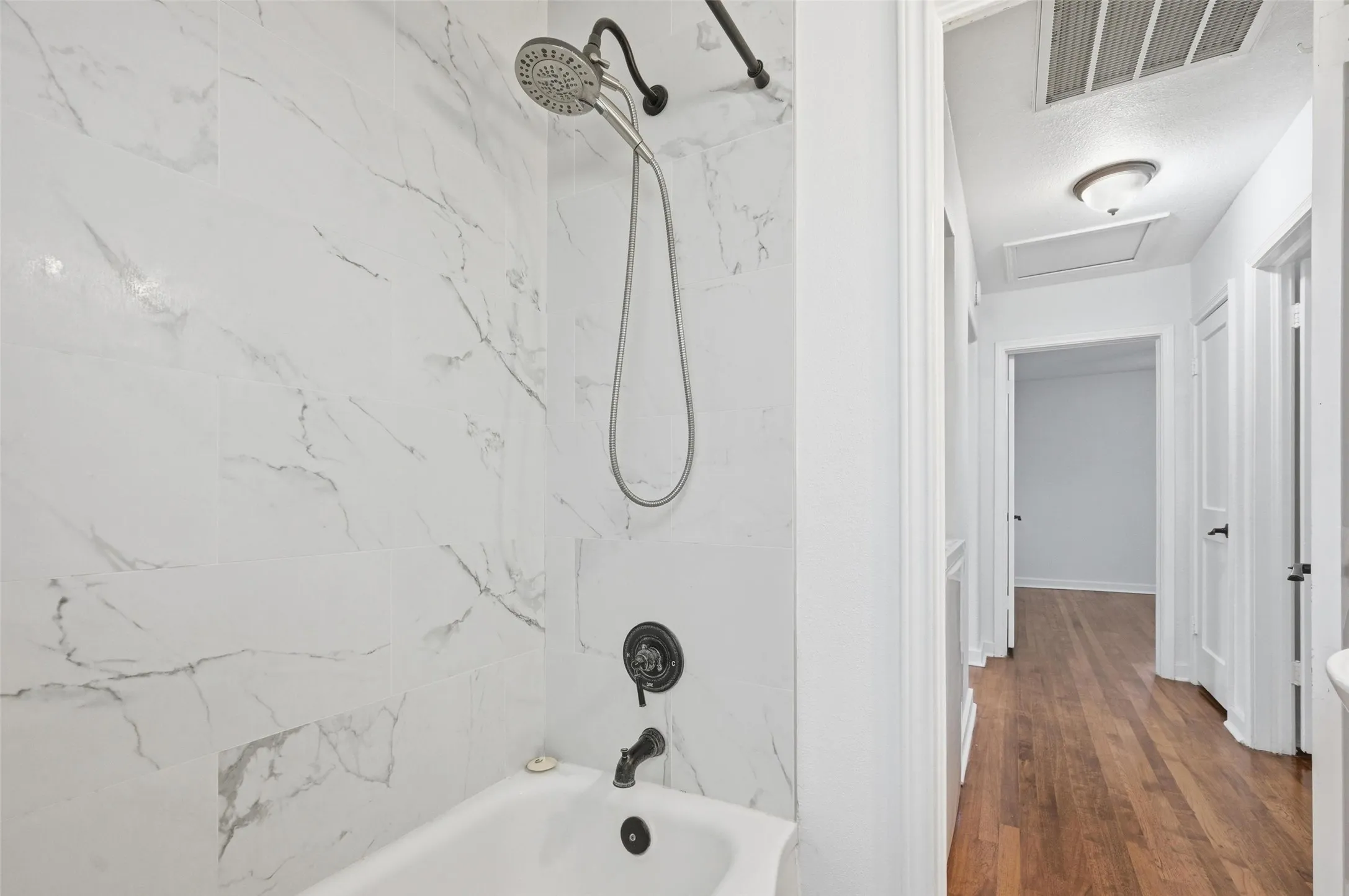 Full bath with washtub / shower combination and dark wood-style flooring