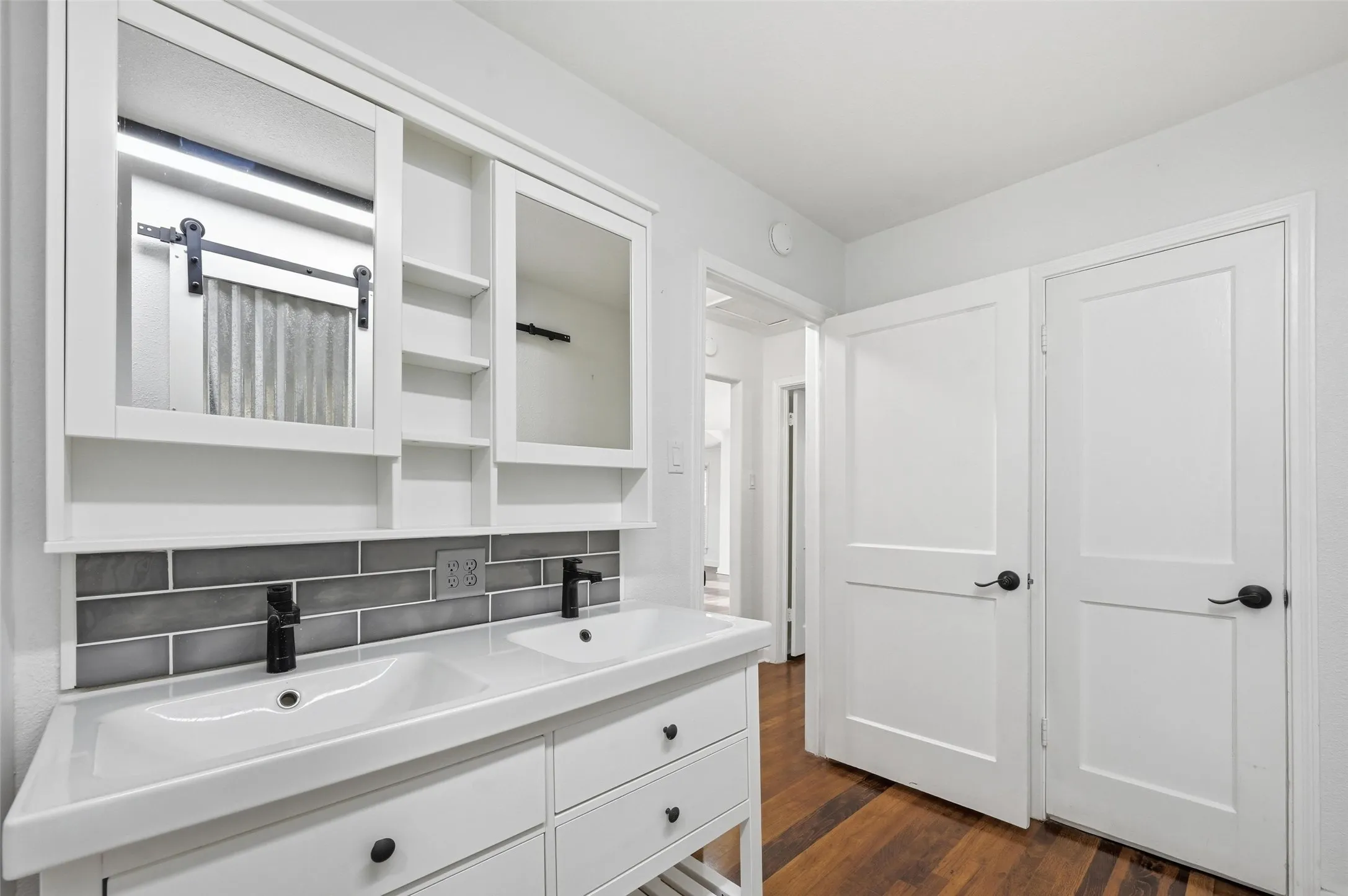 Full bath featuring double vanity, dark wood-style floors, and backsplash
