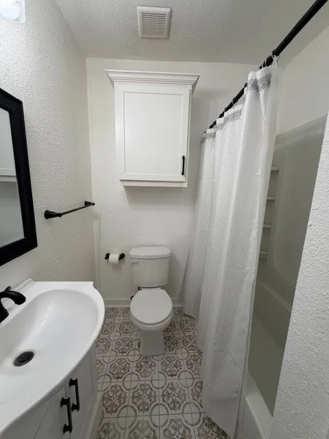 Full bath featuring a textured wall, vanity, a textured ceiling, and shower / tub combo
