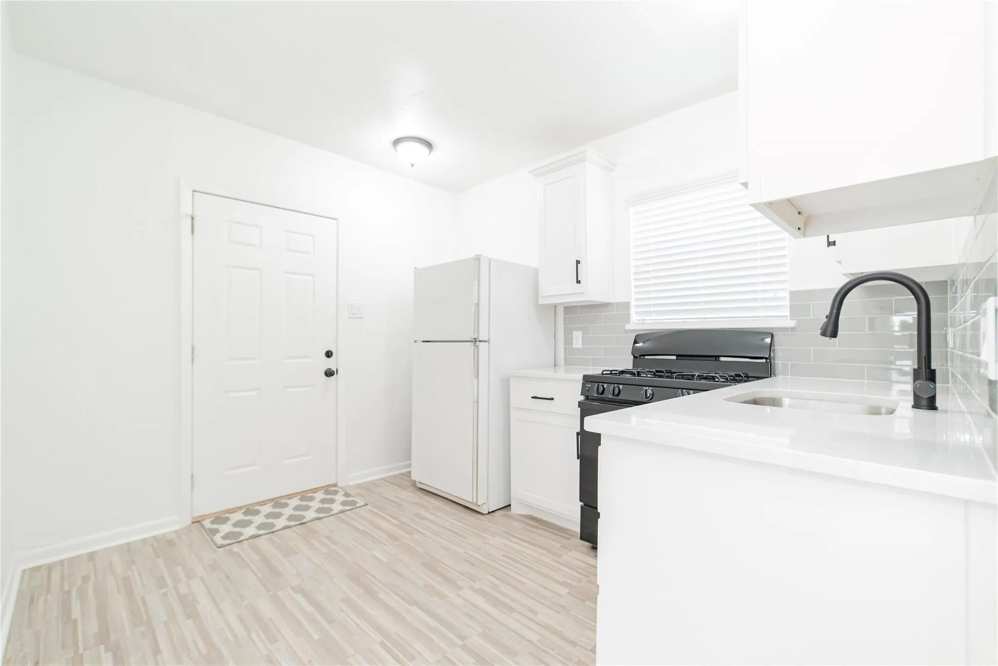 Kitchen featuring gas stove, white cabinets, light wood-style floors, freestanding refrigerator, and backsplash