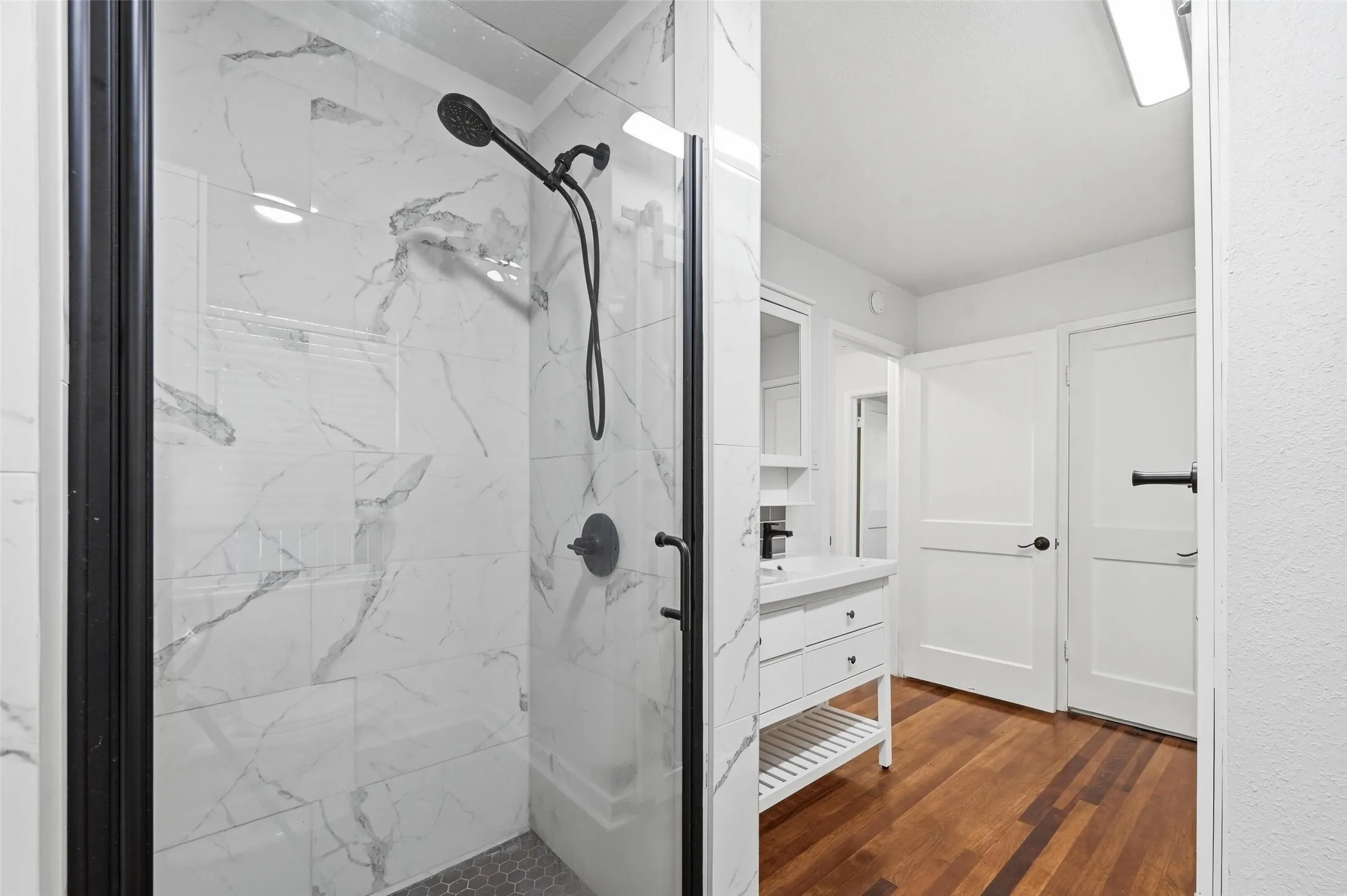 Bathroom with a marble finish shower, dark wood finished floors, and vanity