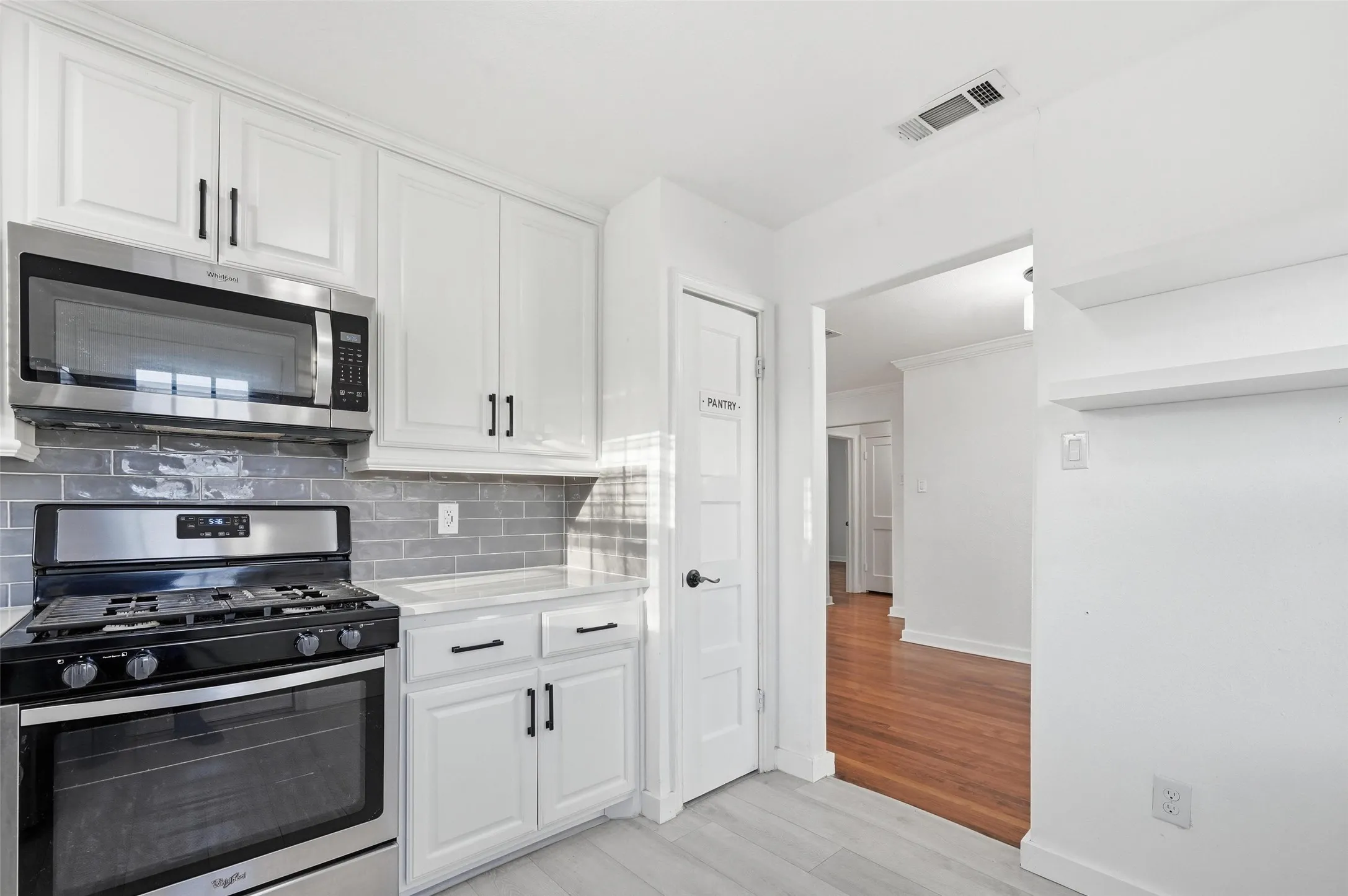 Kitchen featuring stainless steel appliances, light wood finished floors, white cabinetry, backsplash, and light stone countertops
