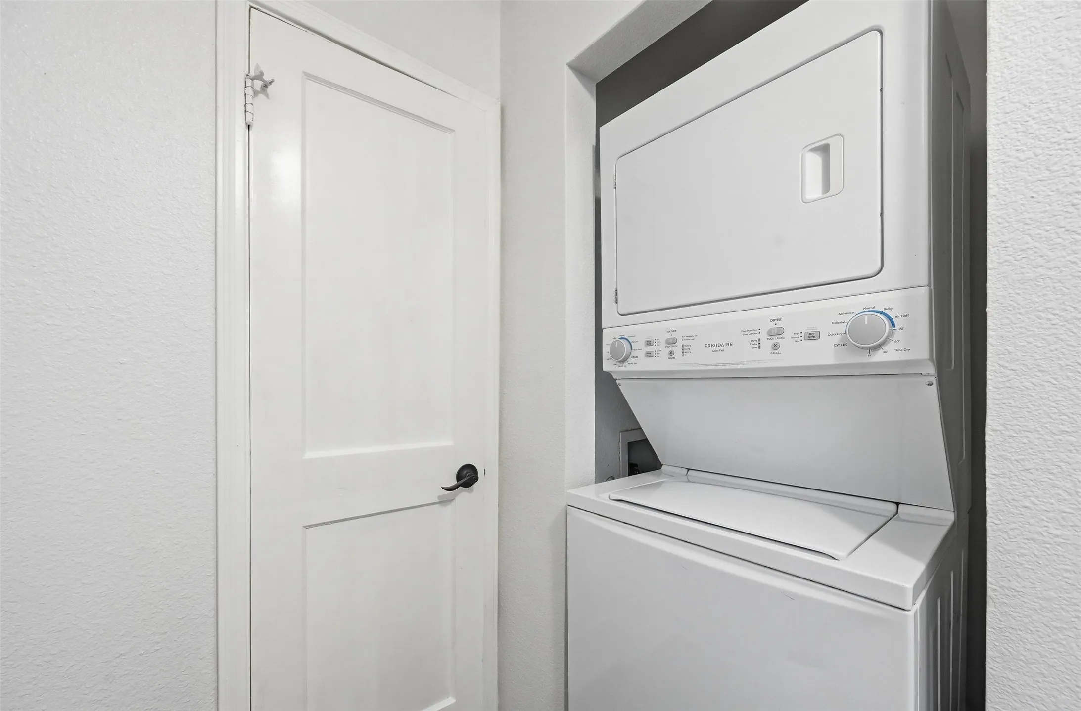 Laundry area with a textured wall and stacked washer / dryer