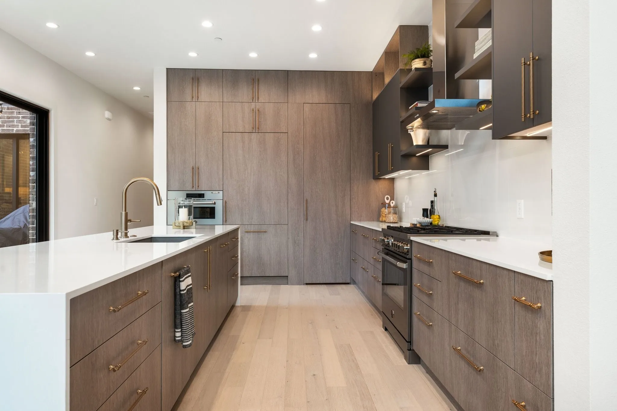 Kitchen featuring high end black range, light quartz stone countertops, waterfall island and hidden pantry