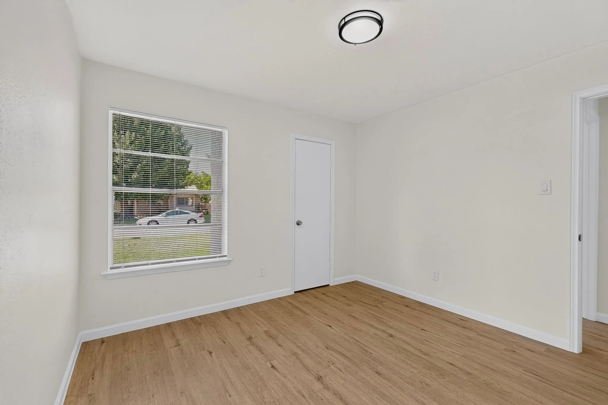 Bright interior space featuring wood-finish flooring, white baseboards, and a window with blinds