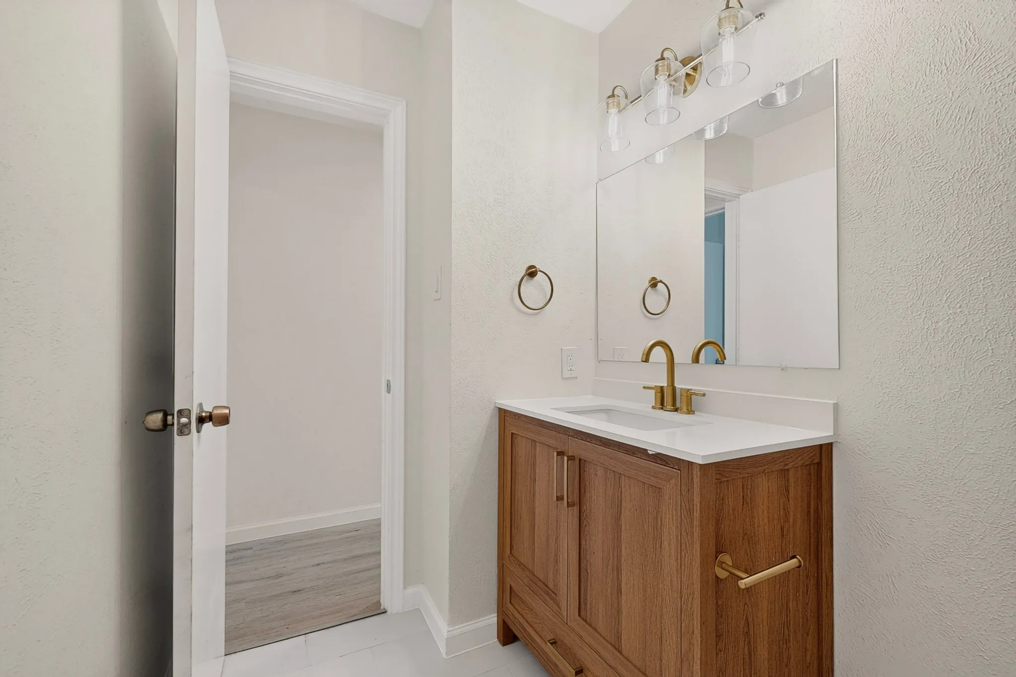 Bathroom featuring a wood-finish vanity with a white countertop, undermount sink, and a gold-tone faucet