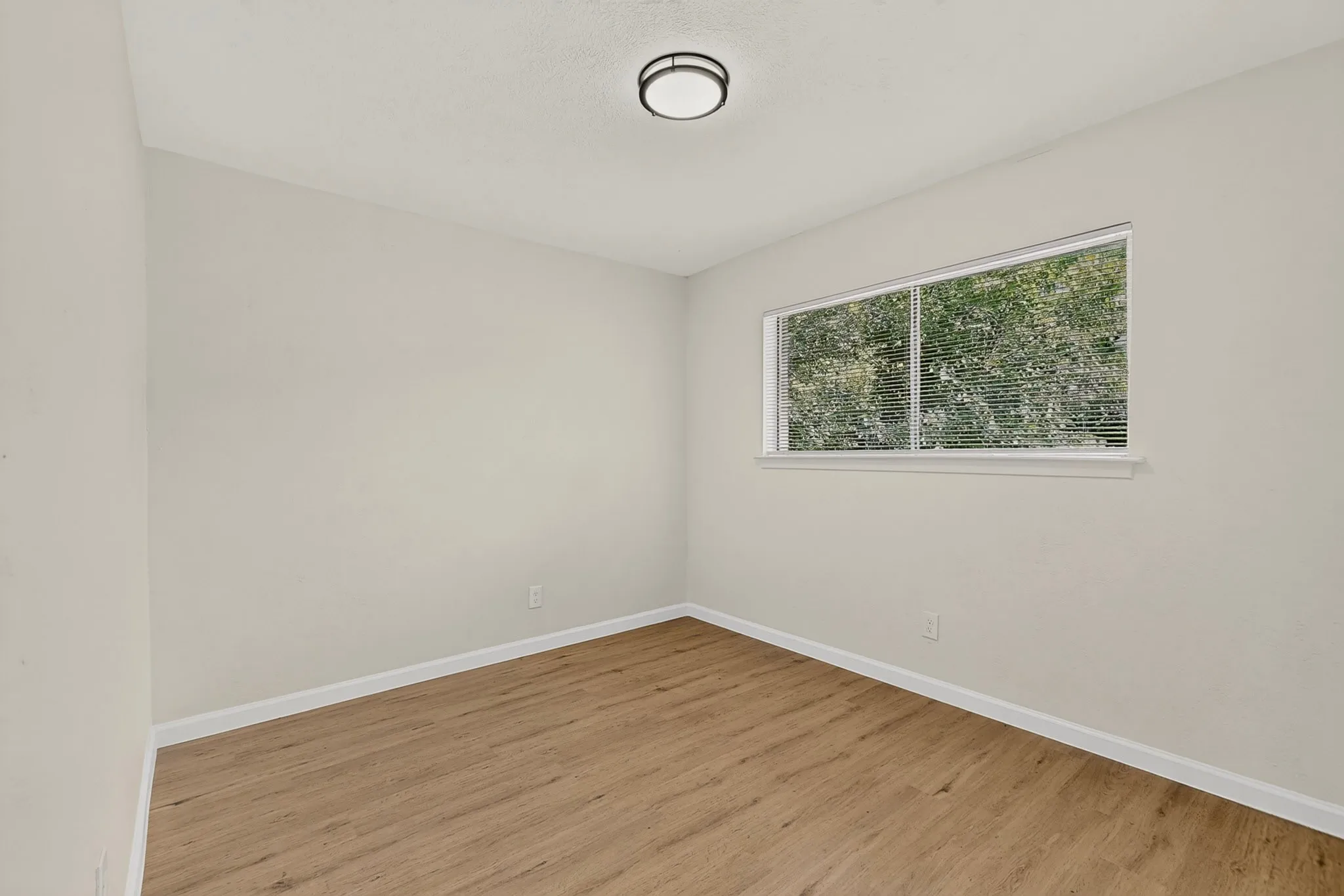 Bright interior room featuring a large window with white blinds, wood-finish flooring, white baseboards, and a contemporary ceiling light fixture