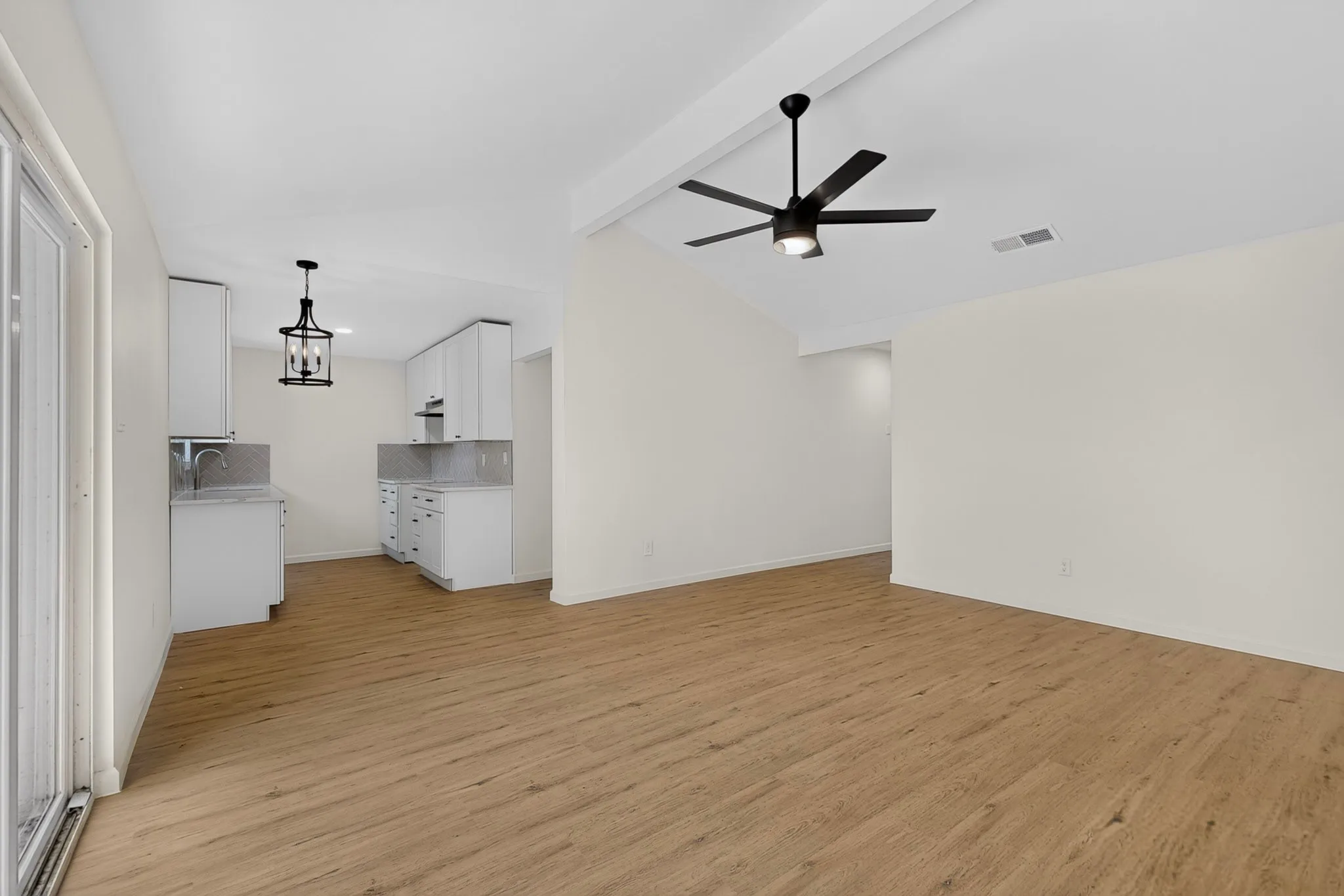 Open-concept living space featuring wood-finish flooring, white walls, and a contemporary black ceiling fan