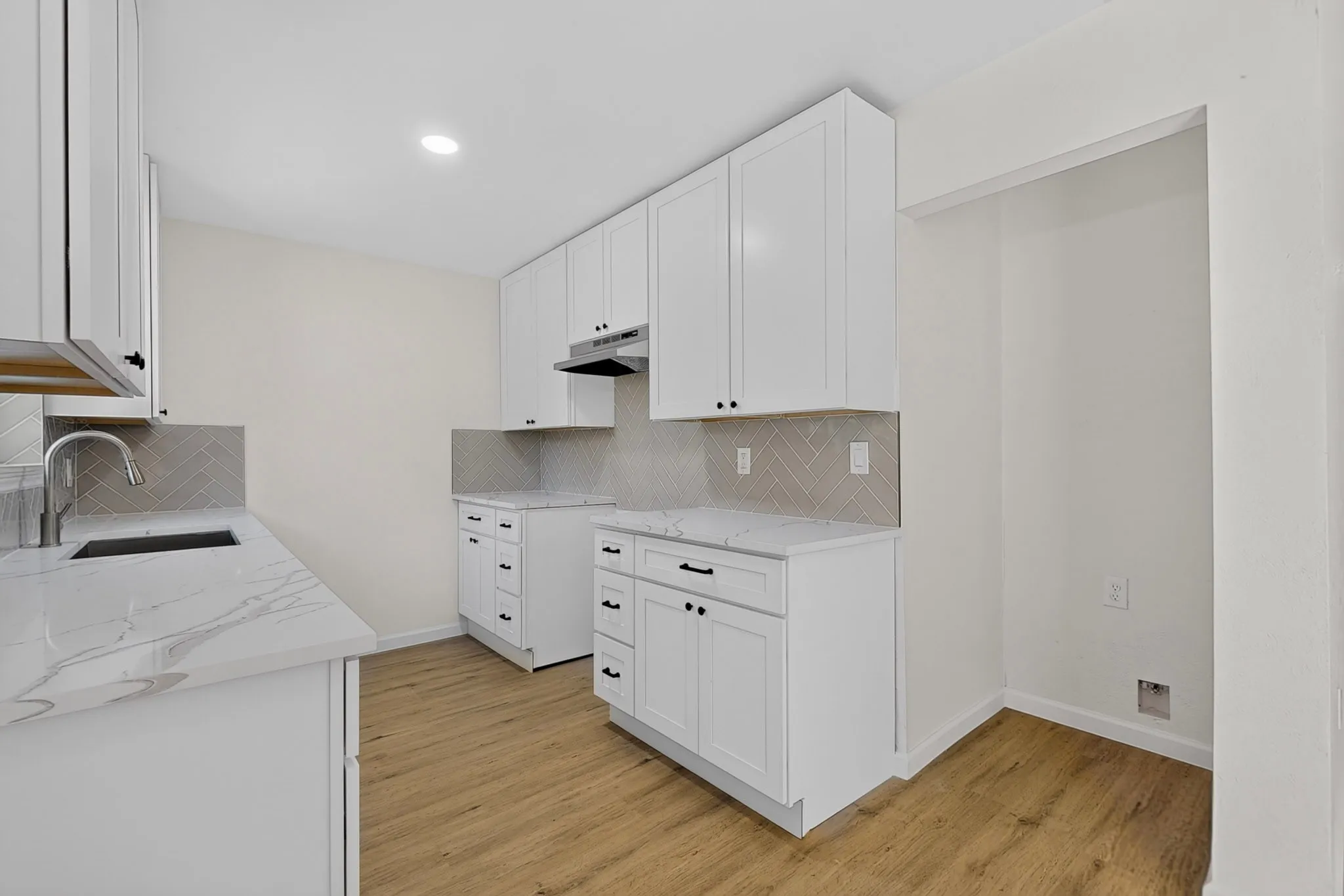 Contemporary kitchen featuring white shaker cabinetry, patterned backsplash, light-toned wood-finish flooring, and recessed lighting
