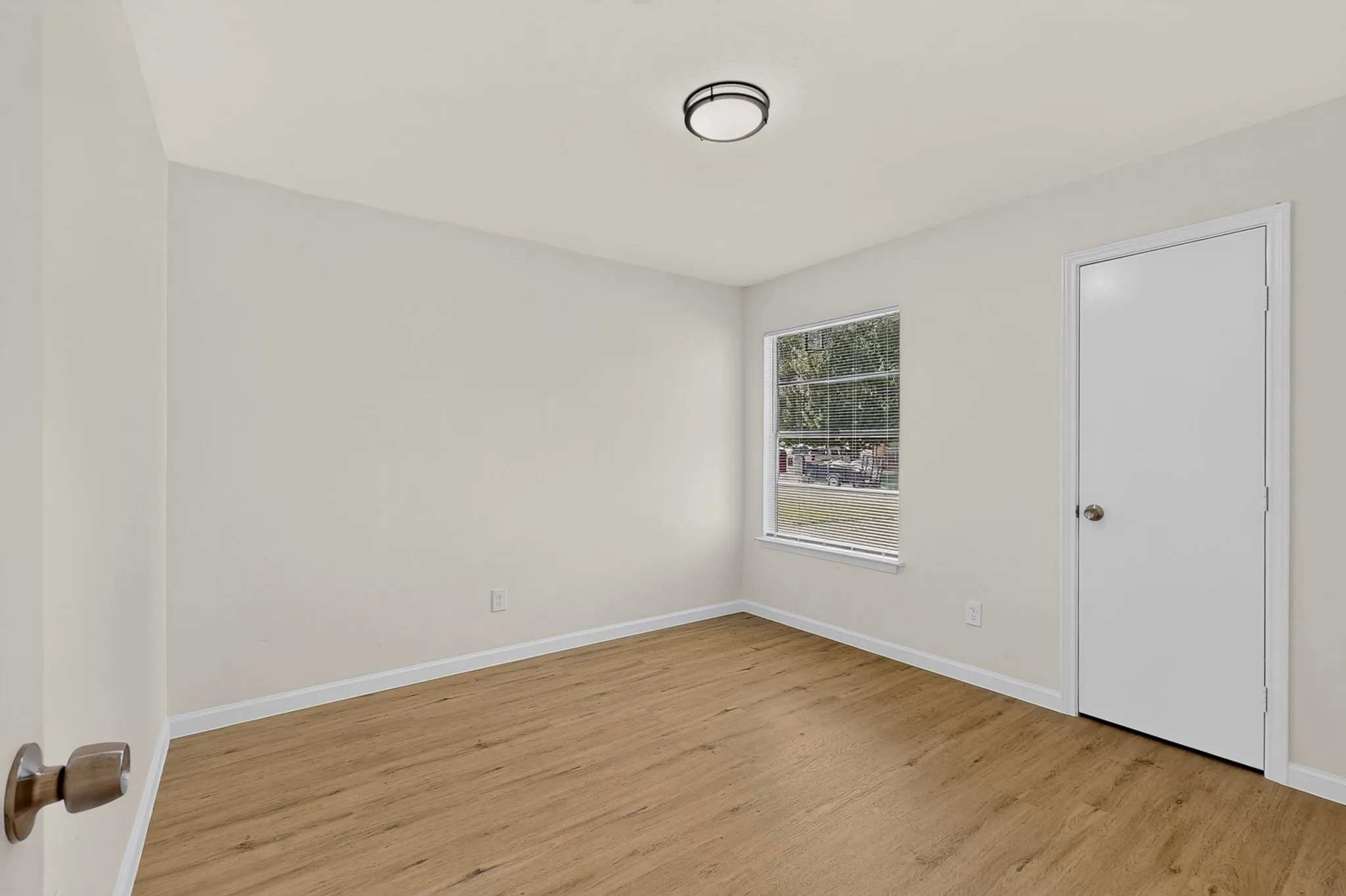 Light-filled interior space featuring wood-finish flooring, white baseboards, and a flush-mount ceiling light