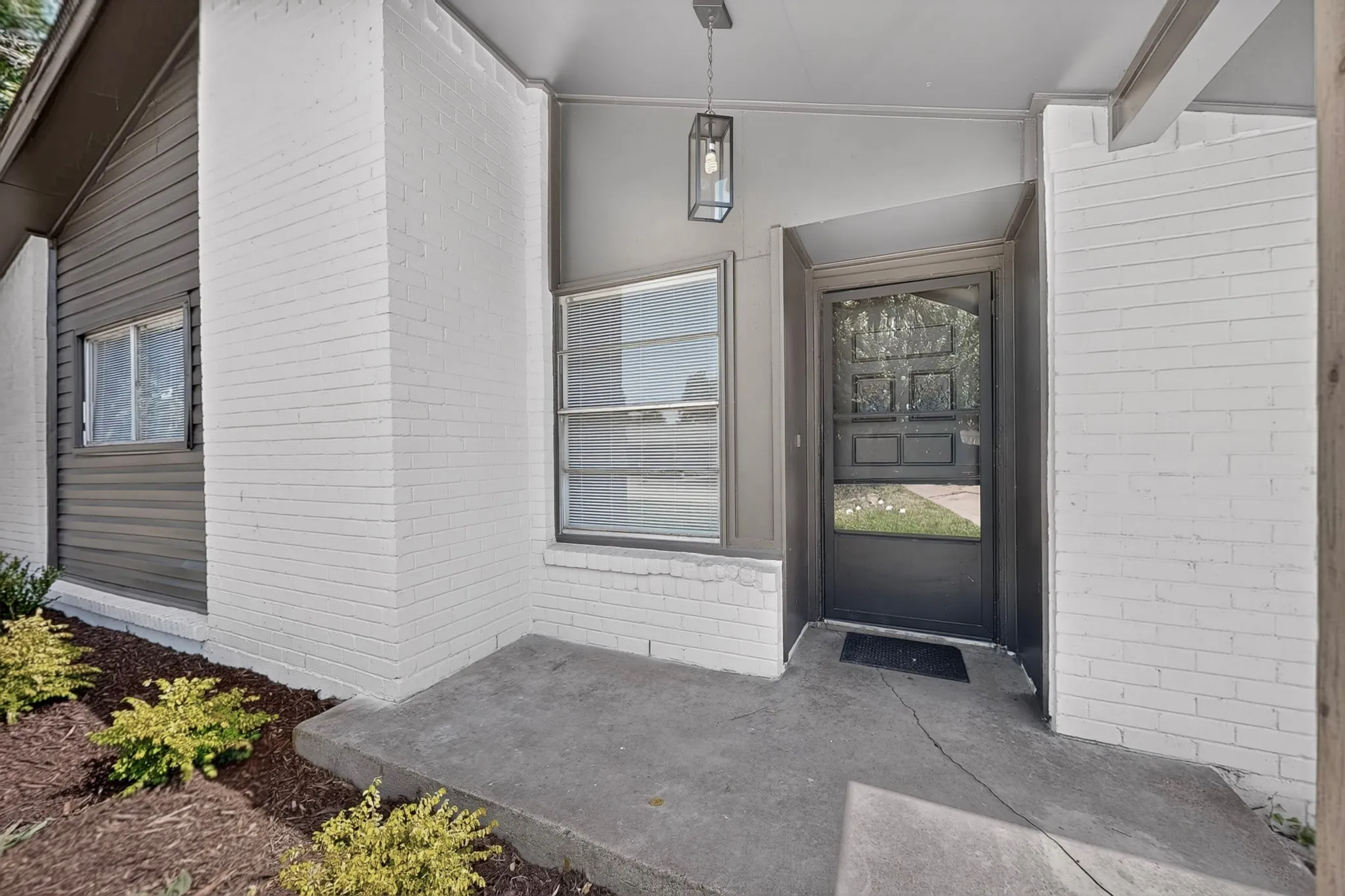 Covered entryway featuring a modern hanging lantern fixture, painted brick facade, and a dark-frame storm door