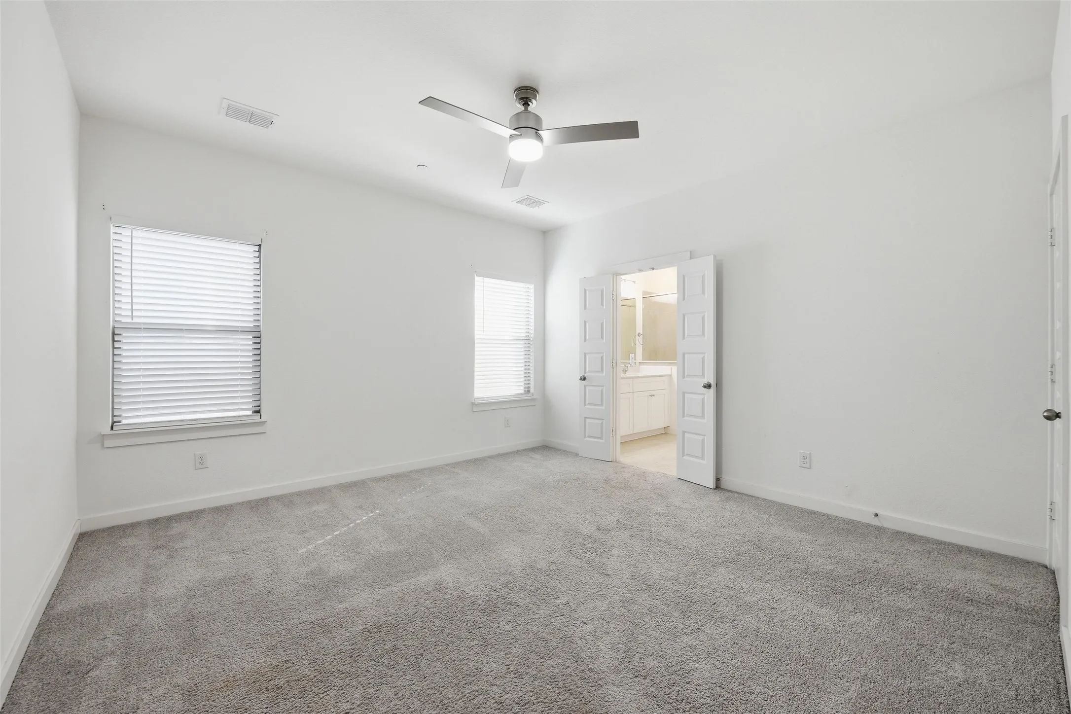 Unfurnished bedroom featuring light carpet, a ceiling fan, and ensuite bath