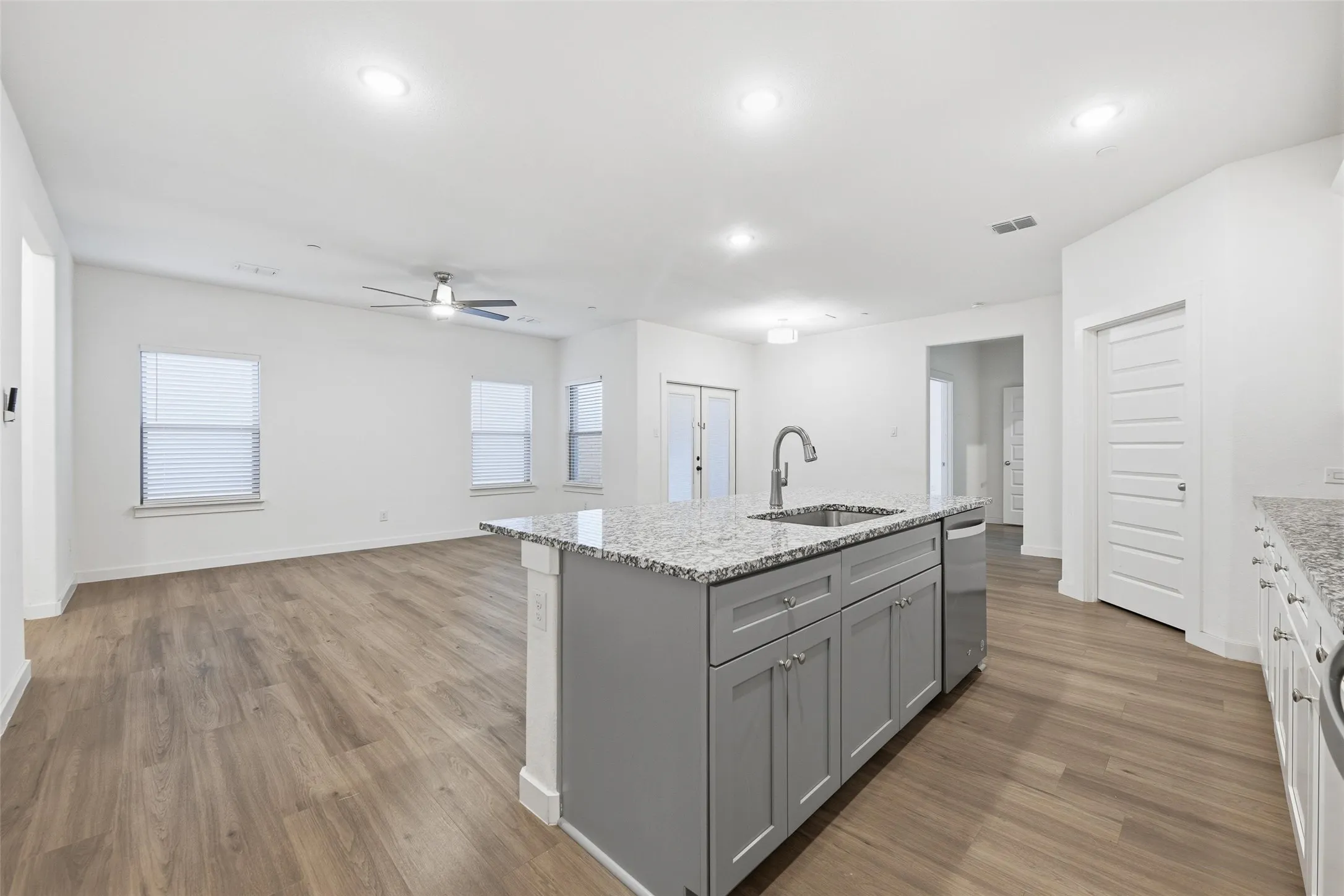 Kitchen with light stone countertops, an island with sink, open floor plan, a ceiling fan, and light wood-style flooring