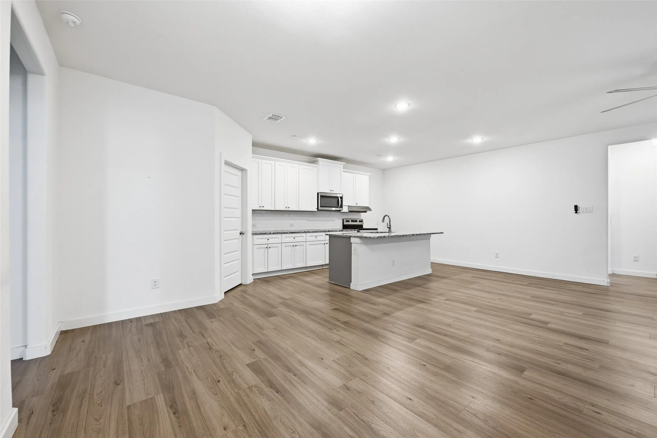 Kitchen featuring open floor plan, white cabinets, a kitchen island with sink, dark wood finished floors, and recessed lighting