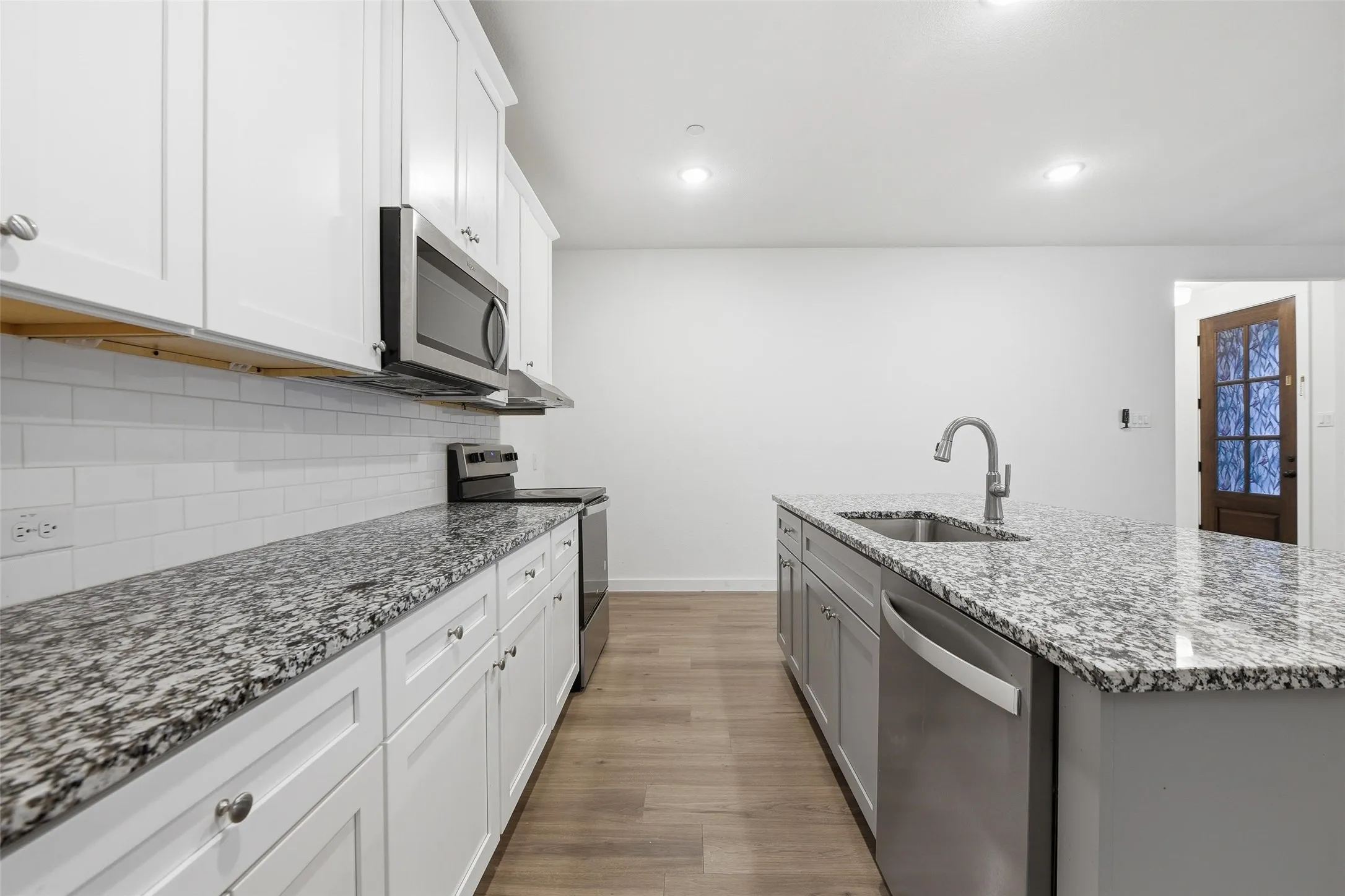 Kitchen with dual tone cabinets, dark stone countertops, stainless steel appliances, light wood finished floors, and a center island with sink